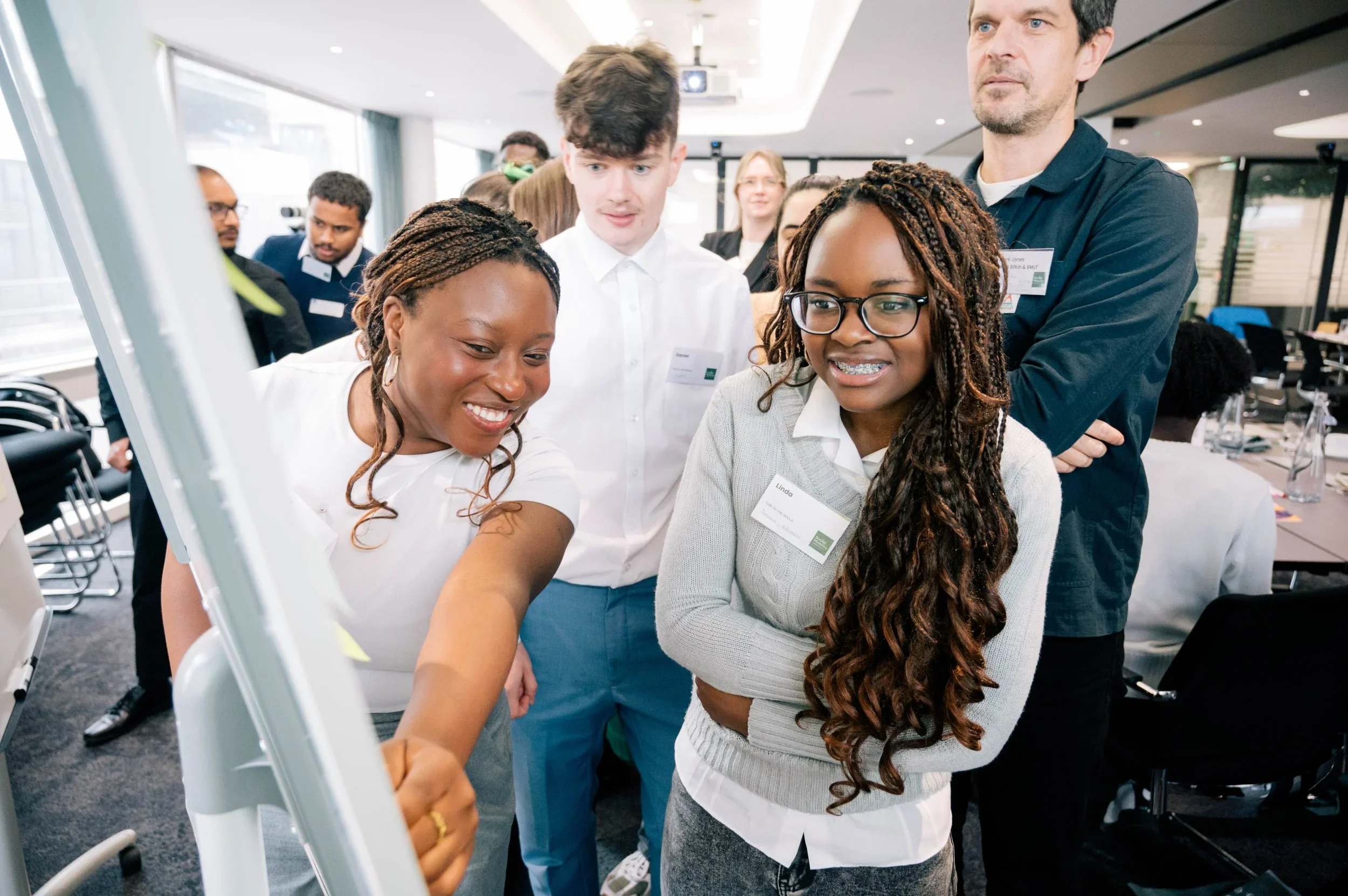 Photograph shows diverse coworkers gathered around a large interactive display during a professional workshop.
