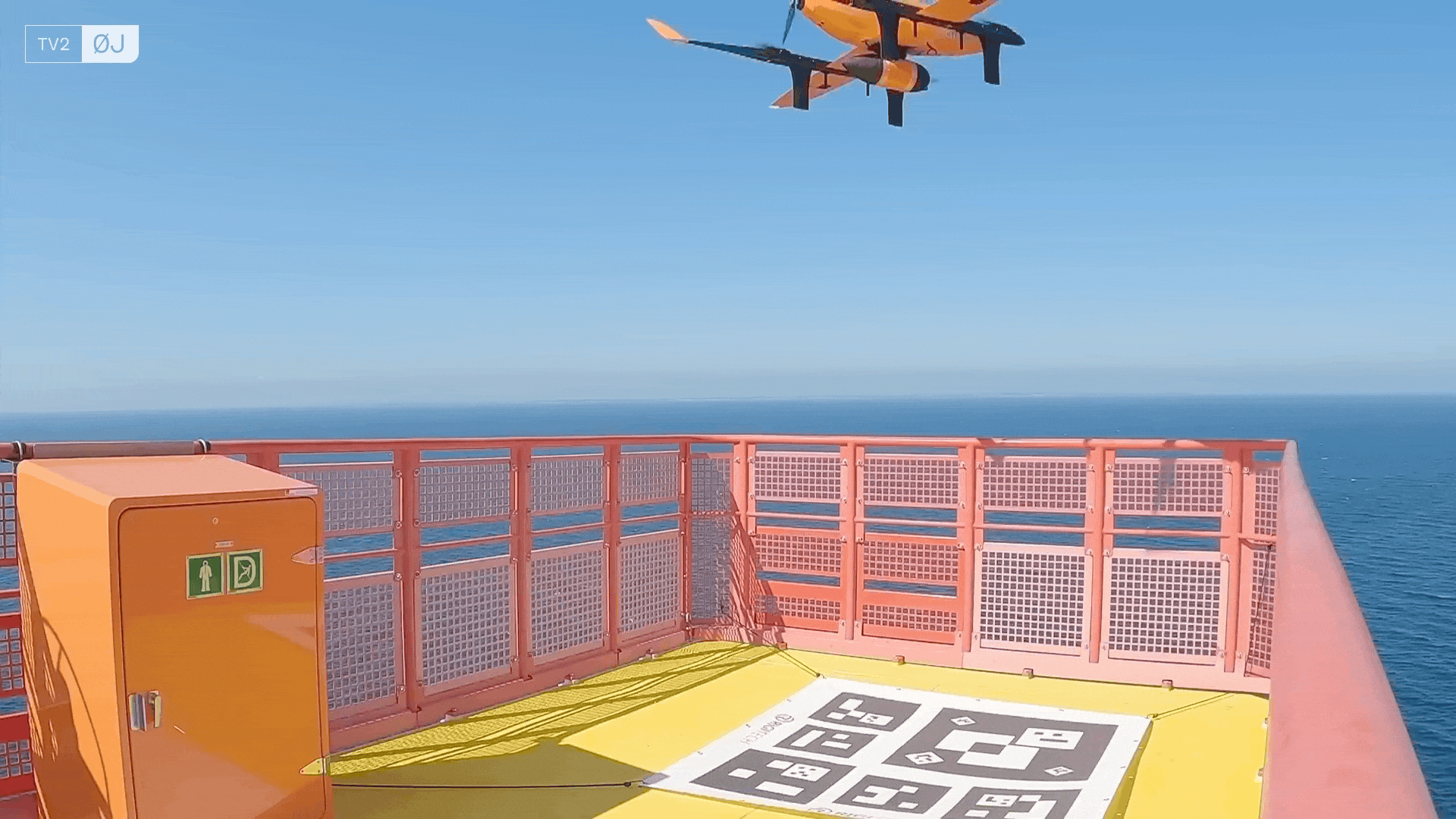 View from a ship's bright pink deck overlooking the ocean, with a portable orange emergency kit and a hopscotch game painted on the yellow floor near a safety railing.