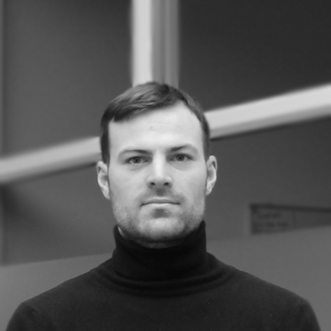 Black and white portrait of a man with short hair, wearing a turtleneck sweater, looking directly at the camera with a neutral expression.
