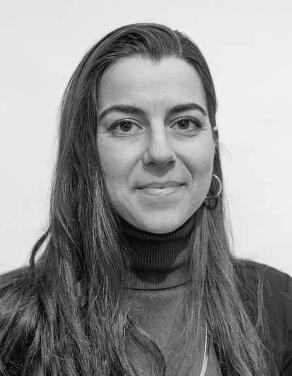 Black-and-white portrait of a woman with long hair, wearing a turtleneck and earrings, smiling slightly, against a plain background.