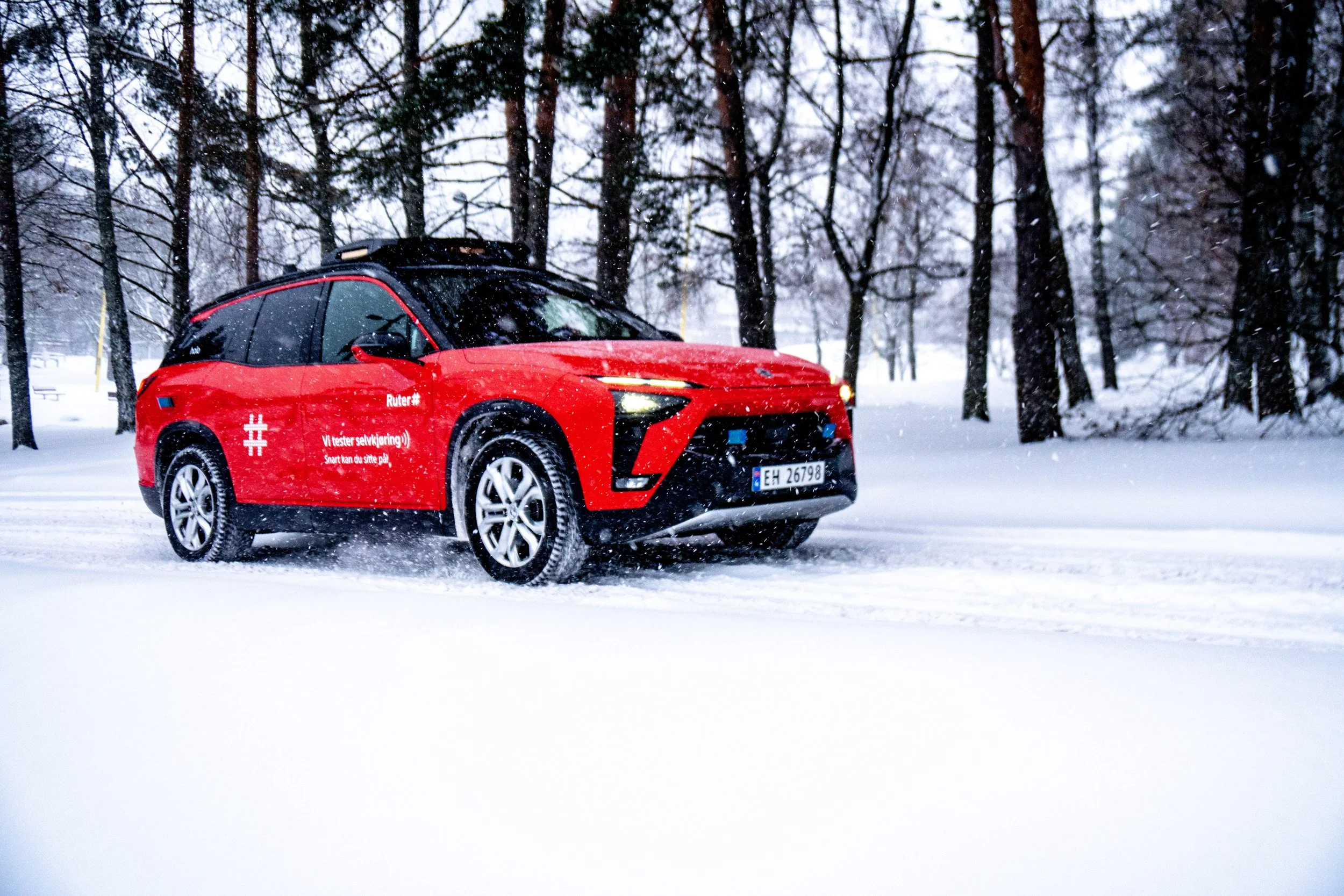 Red autonomous Holo vehicle driving through a snowy landscape with trees in the background.