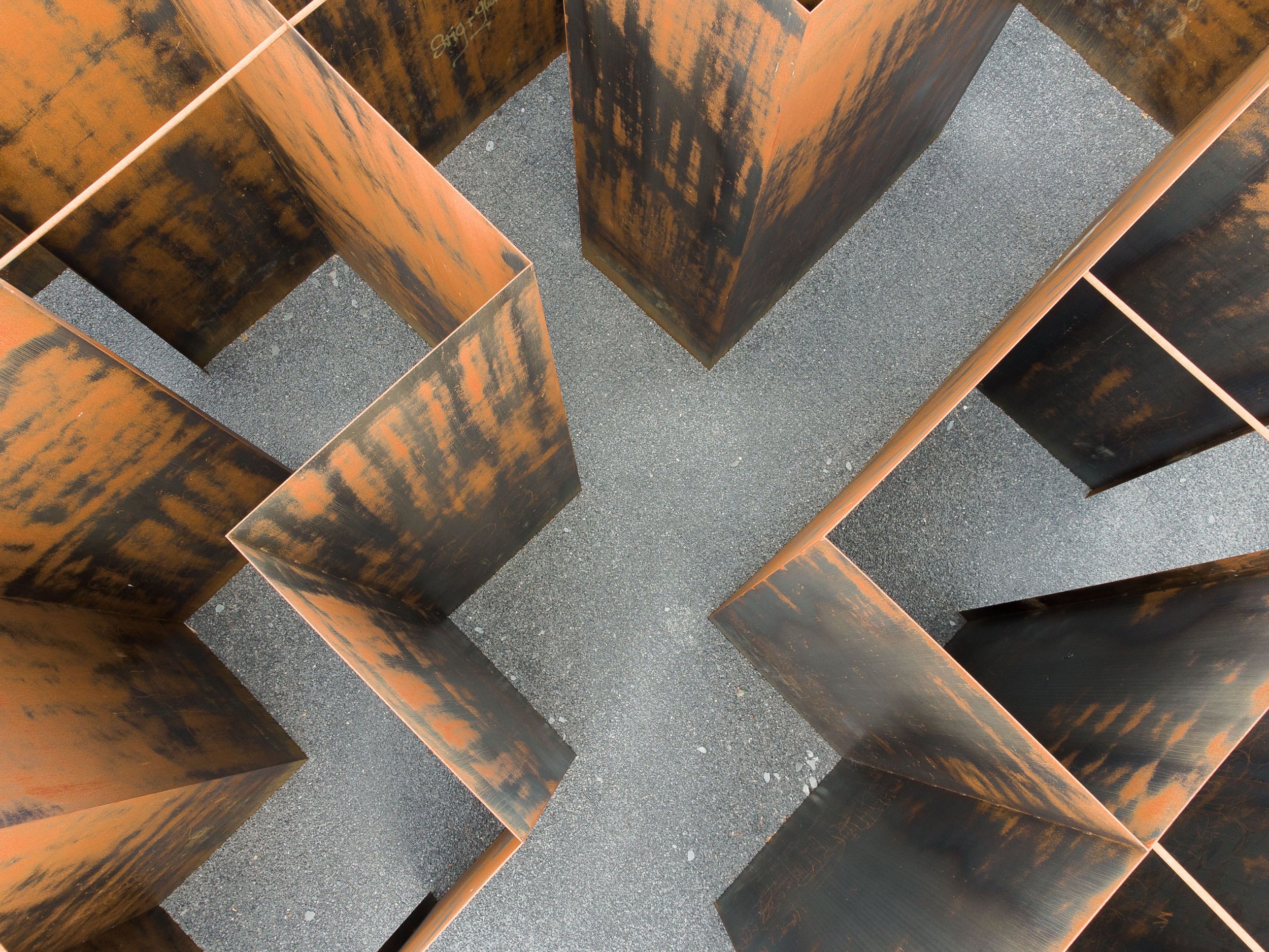 Specialtillverkade detaljer i cortenstål på mått med naturlig rostpatina, fotograferade ovanifrån i geometriskt mönster.