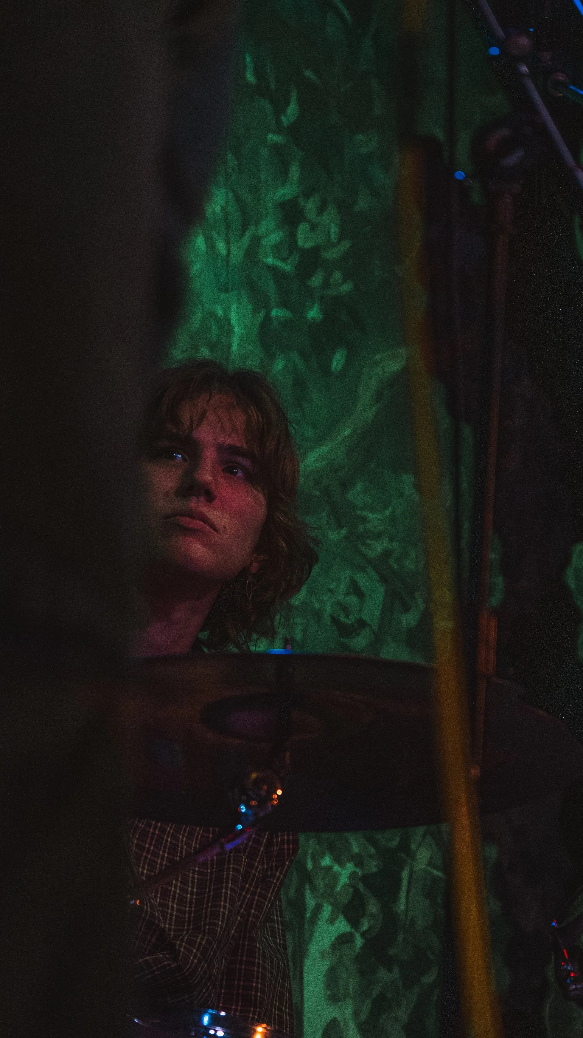 A young woman with short hair looks thoughtful, illuminated by colorful lights in a dark environment.