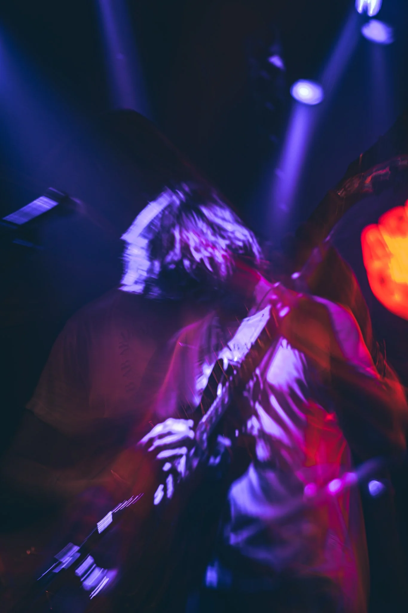 Person playing acoustic guitar in a dark, colorful setting with purple and red lighting.