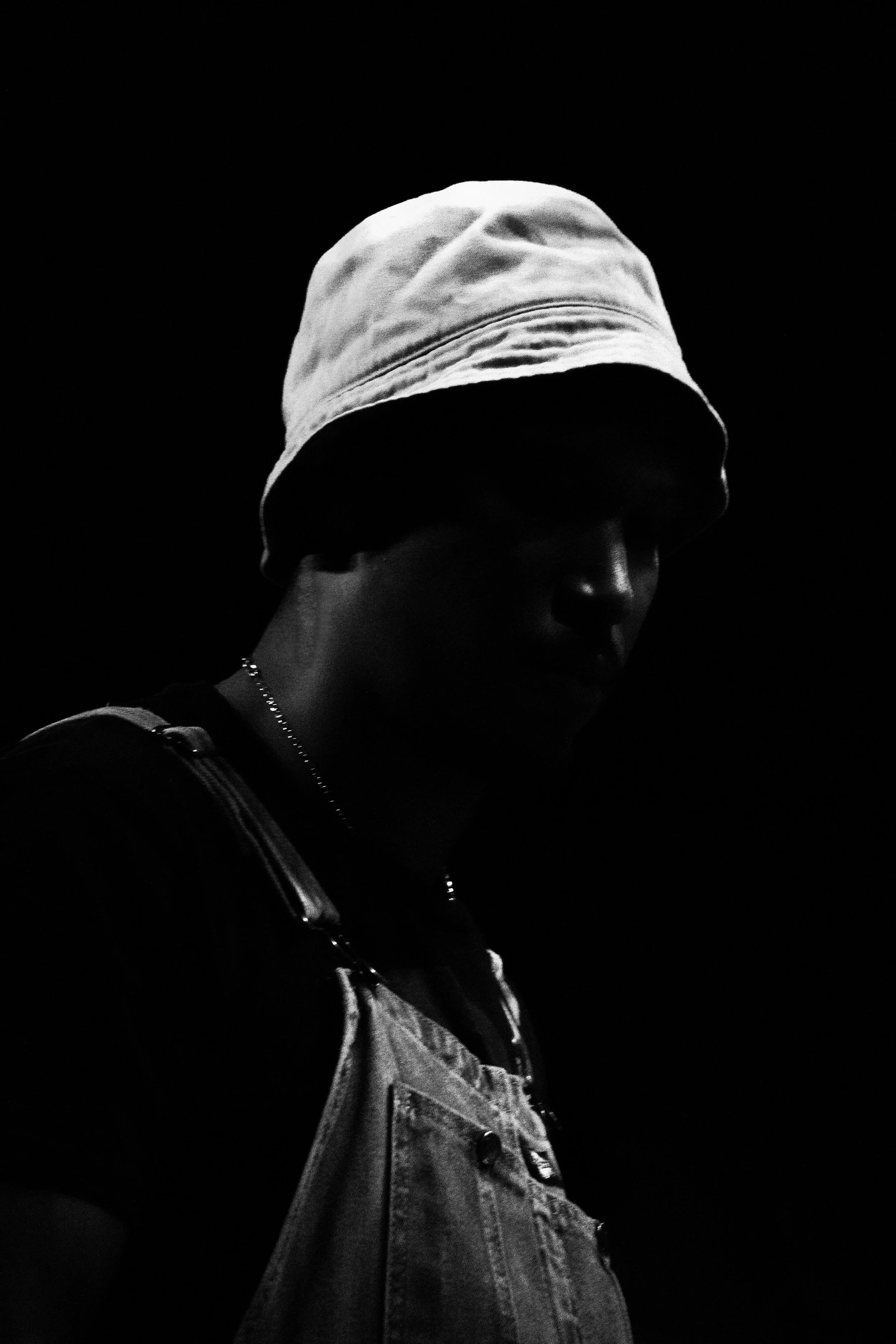 A person wearing a white beanie, denim jacket, and carrying a backpack, walking in a dark environment.