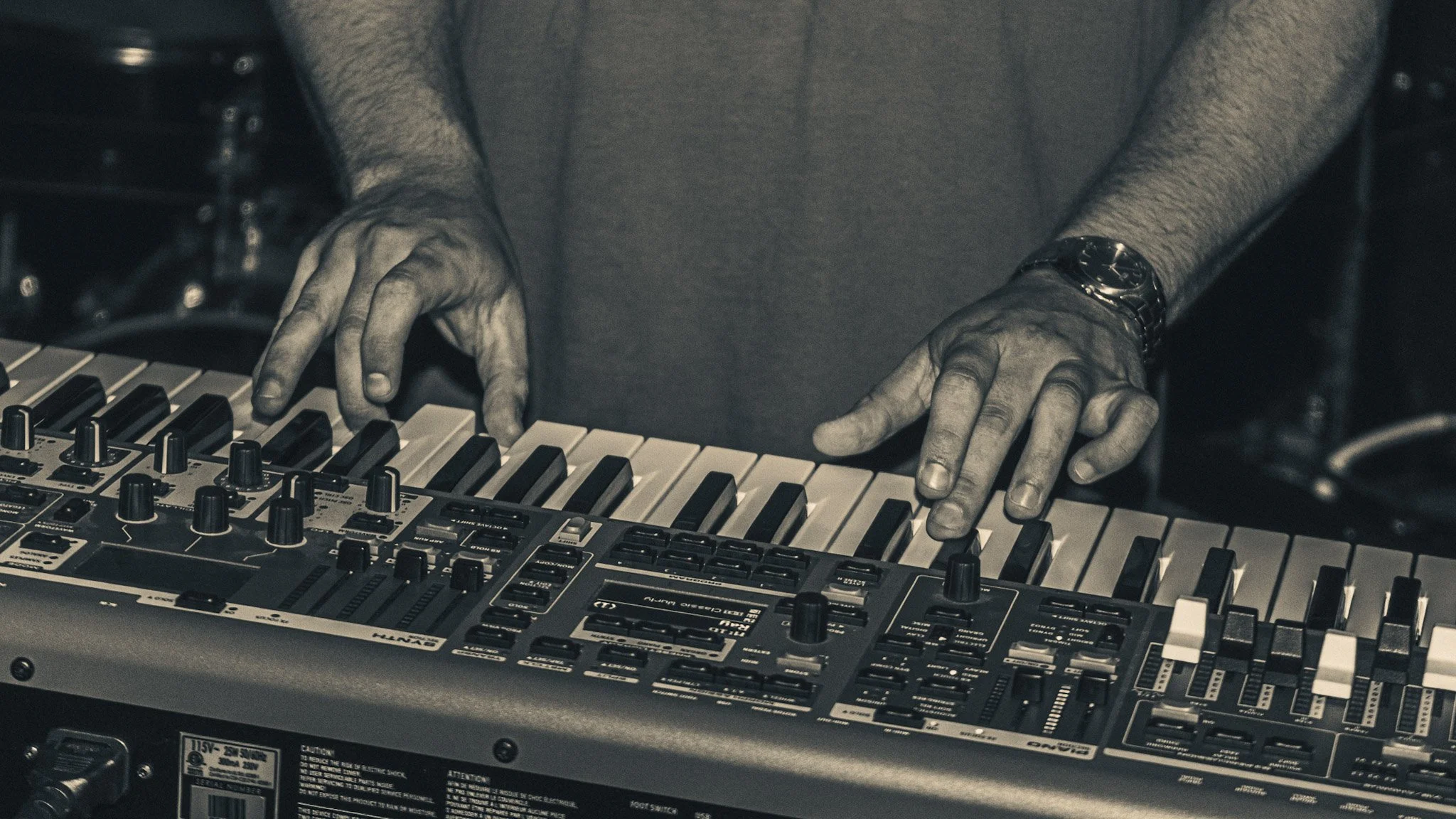 Close-up of a person's hands playing a synthesizer with black and white keys, and various control knobs.