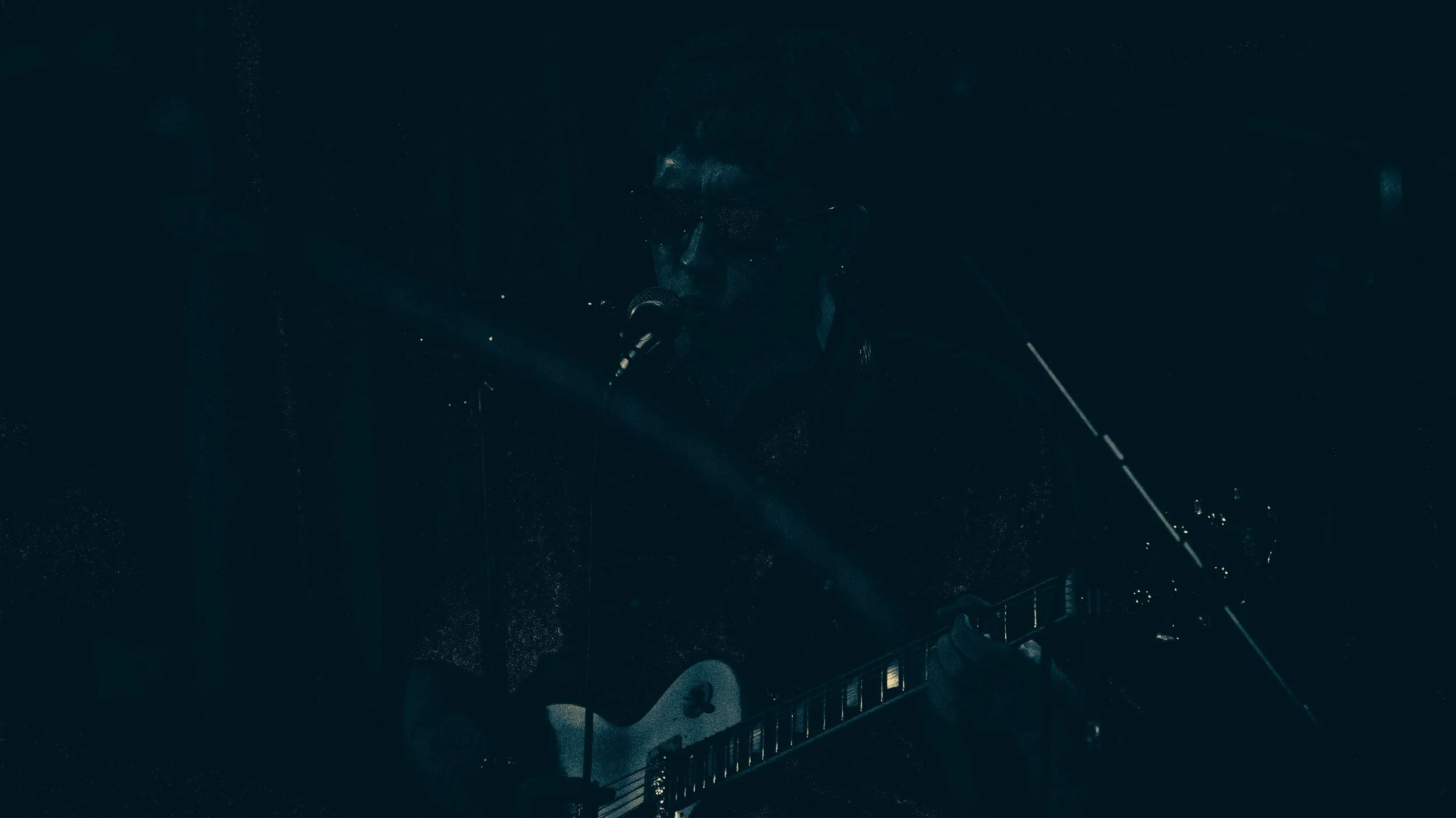 A person on a balcony at night, holding a guitar and singing into a microphone.