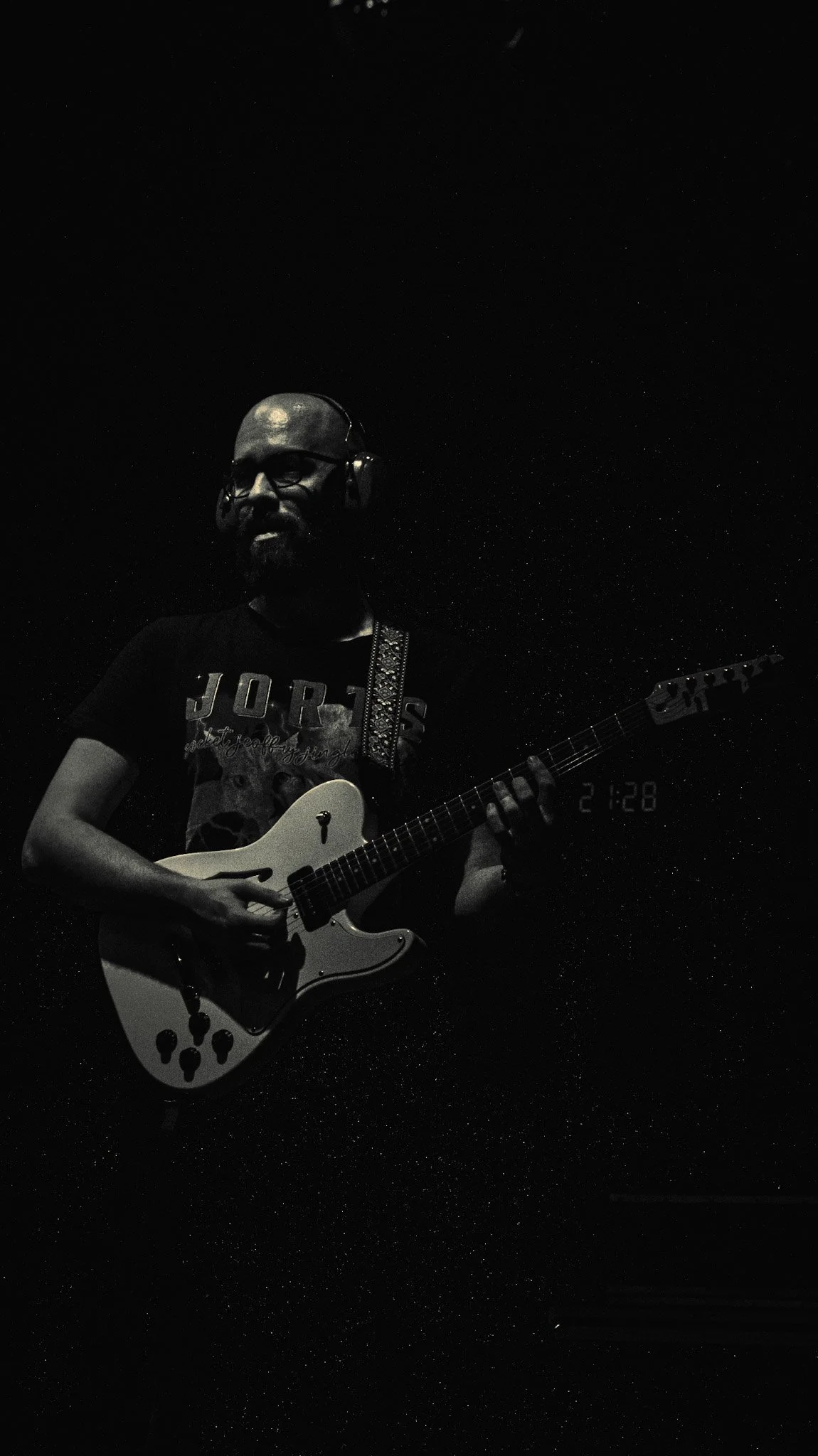 A man wearing glasses and headphones playing an electric guitar in a dark setting, with a starry background and a timestamp of 21:28.