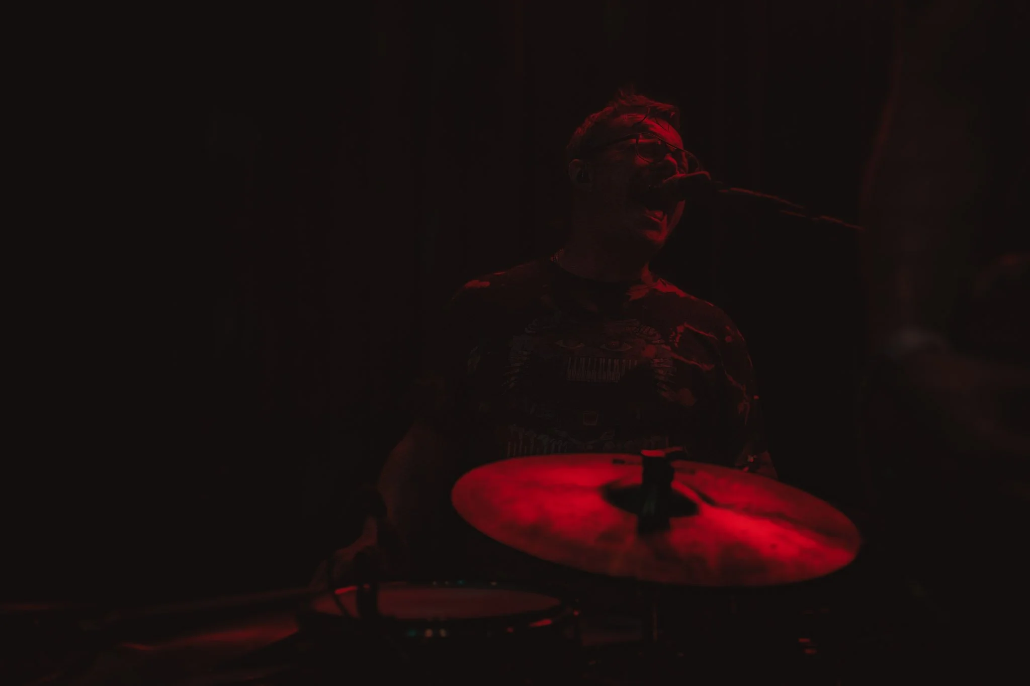 A musician playing drums in a dimly lit environment with red lighting.