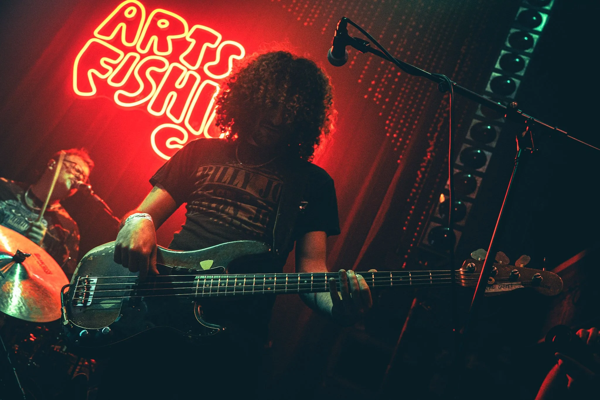 Musician with curly hair playing a bass guitar on stage at Night Shift Music.