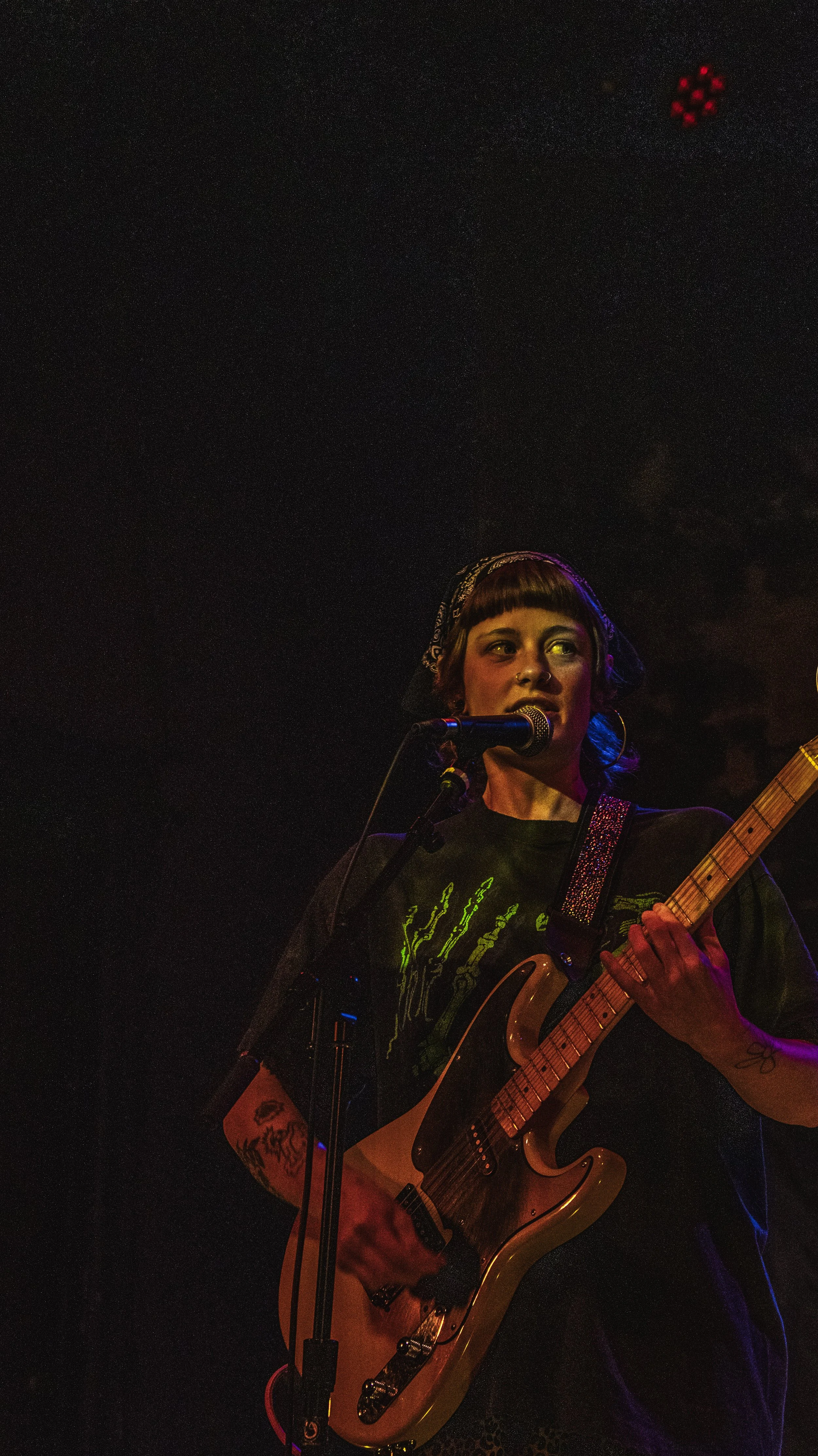 A woman playing an electric guitar and singing into a microphone during a live music performance.
