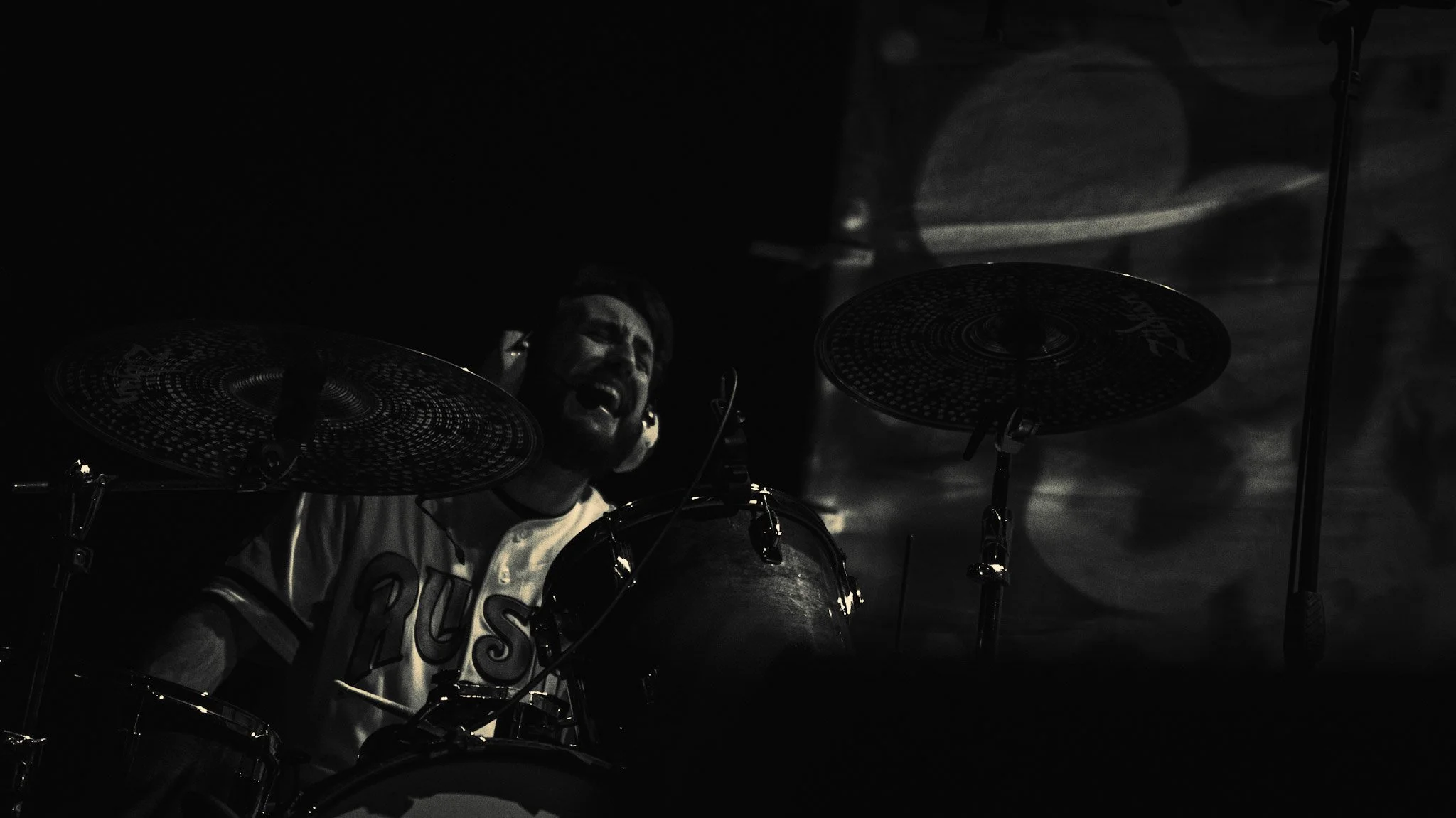 Black and white photograph of a person passionately playing drums with a focused expression, close-up on the face and drum set.
