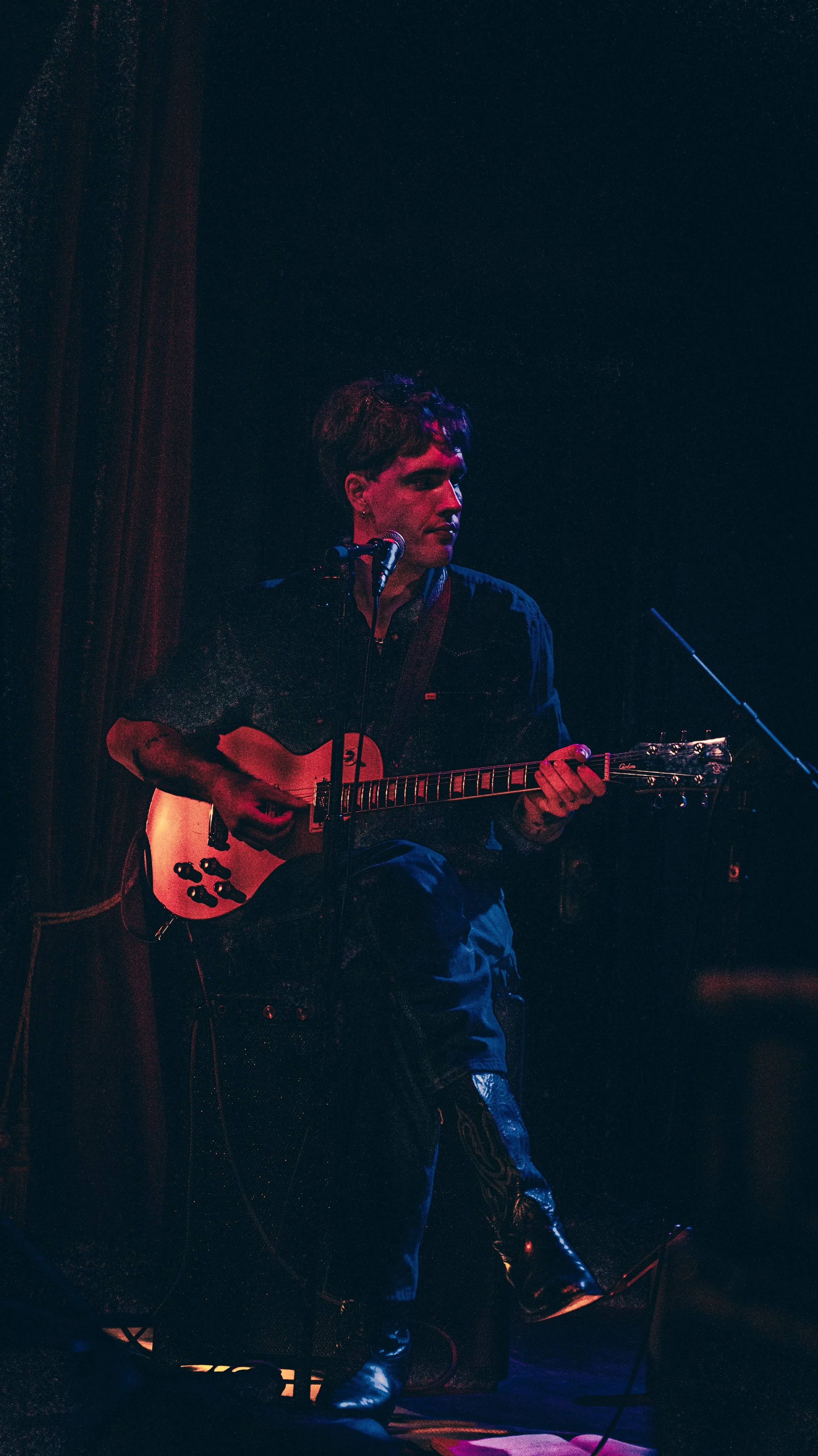 A person playing an electric guitar on stage, with a dark background and colorful lighting.