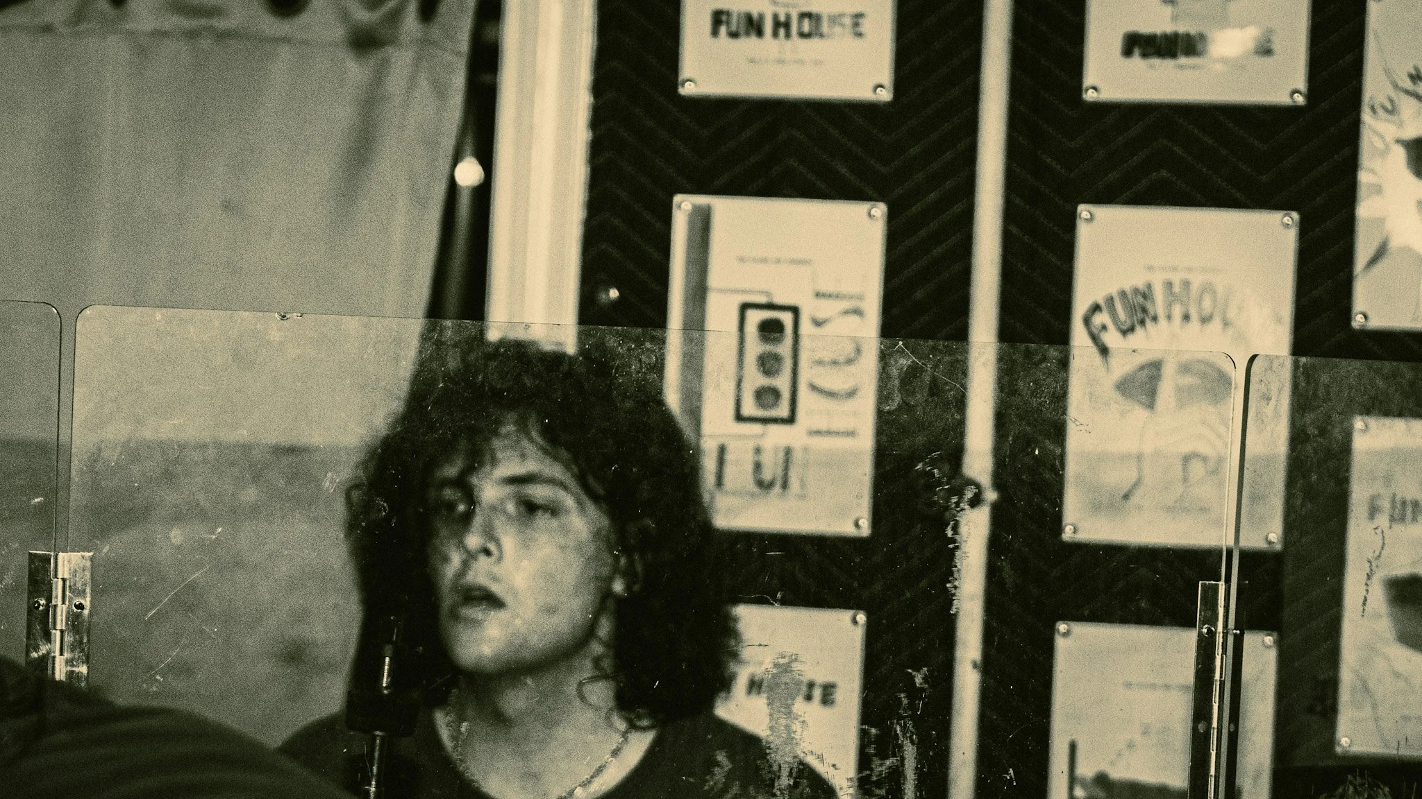 A person with curly hair taking a selfie in front of glass panels with signs containing text and logos.