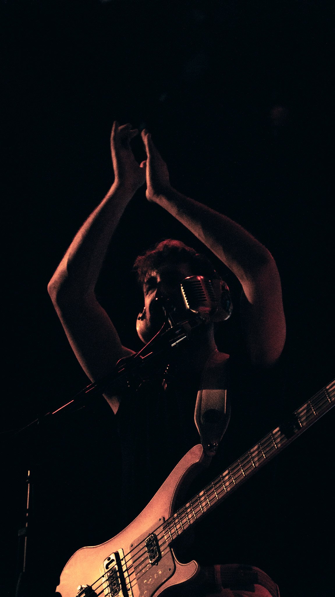 Person wearing headphones, playing an electric guitar, and singing into a microphone in a dark setting.