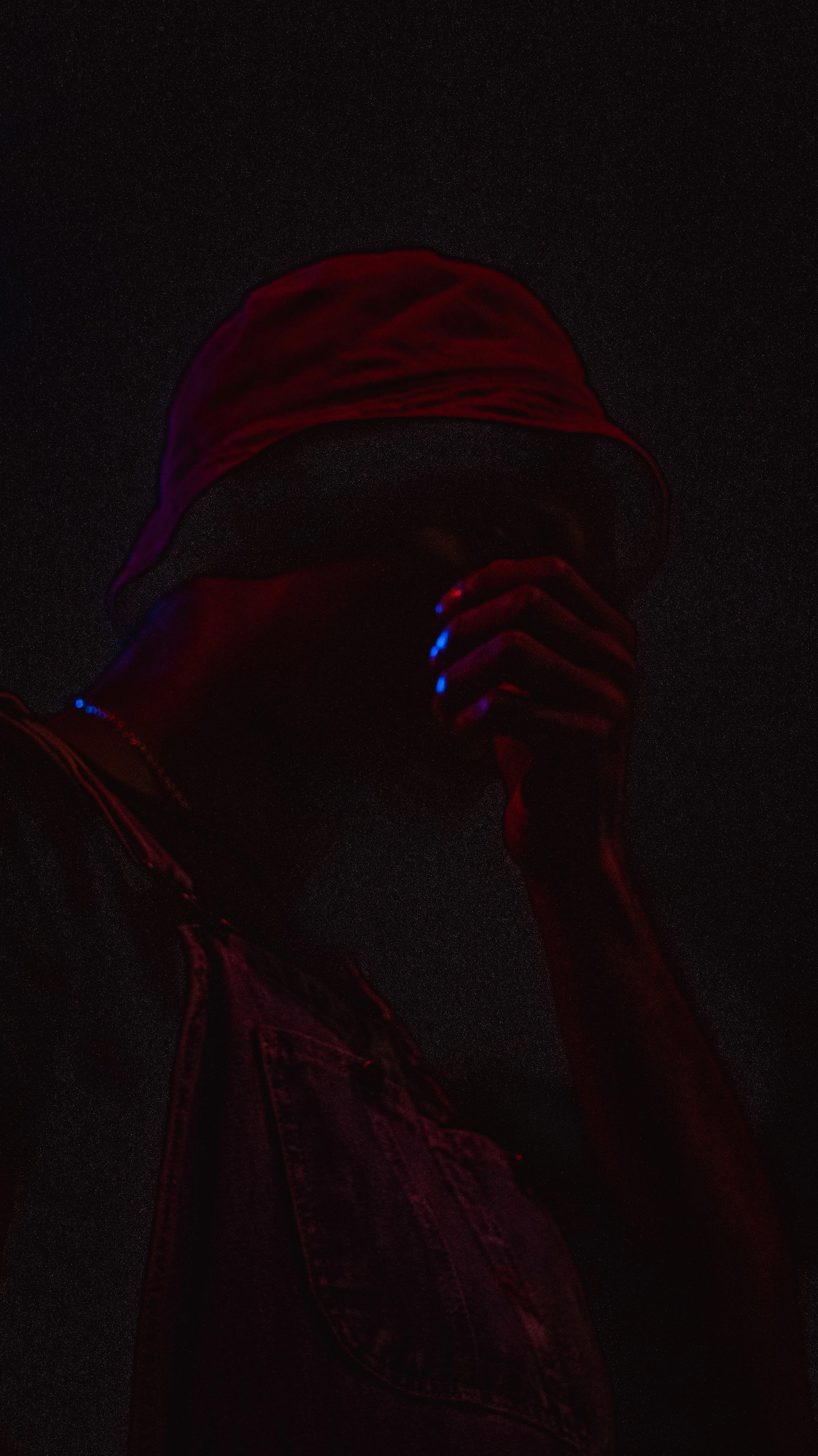 A silhouette of a person wearing a red hat, denim jacket, and hand near face against a starry night sky.