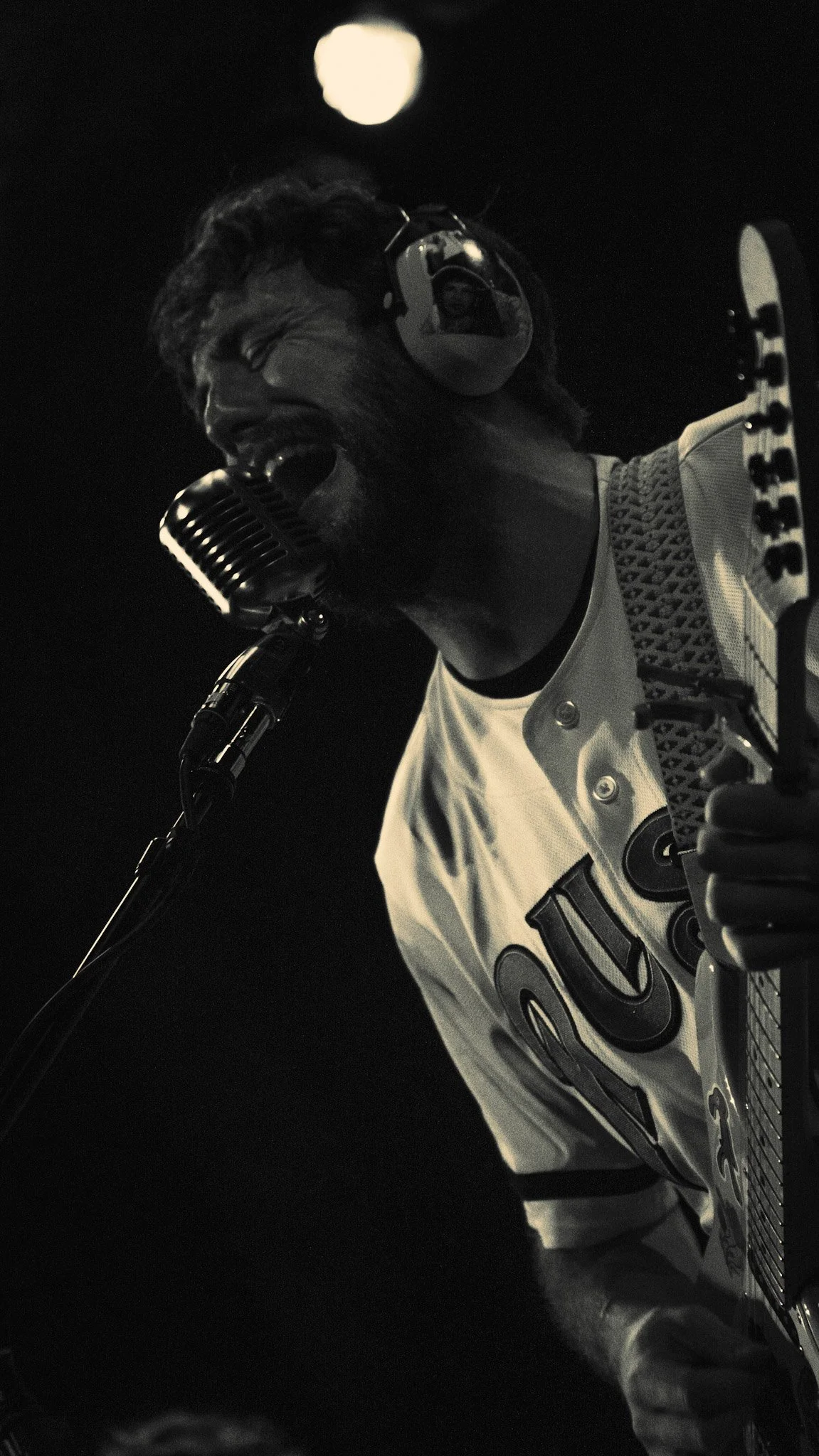A male singer is performing with a vintage microphone. He is wearing headphones and a Harley-Davidson shirt, and he is playing a guitar. The background features a full moon.