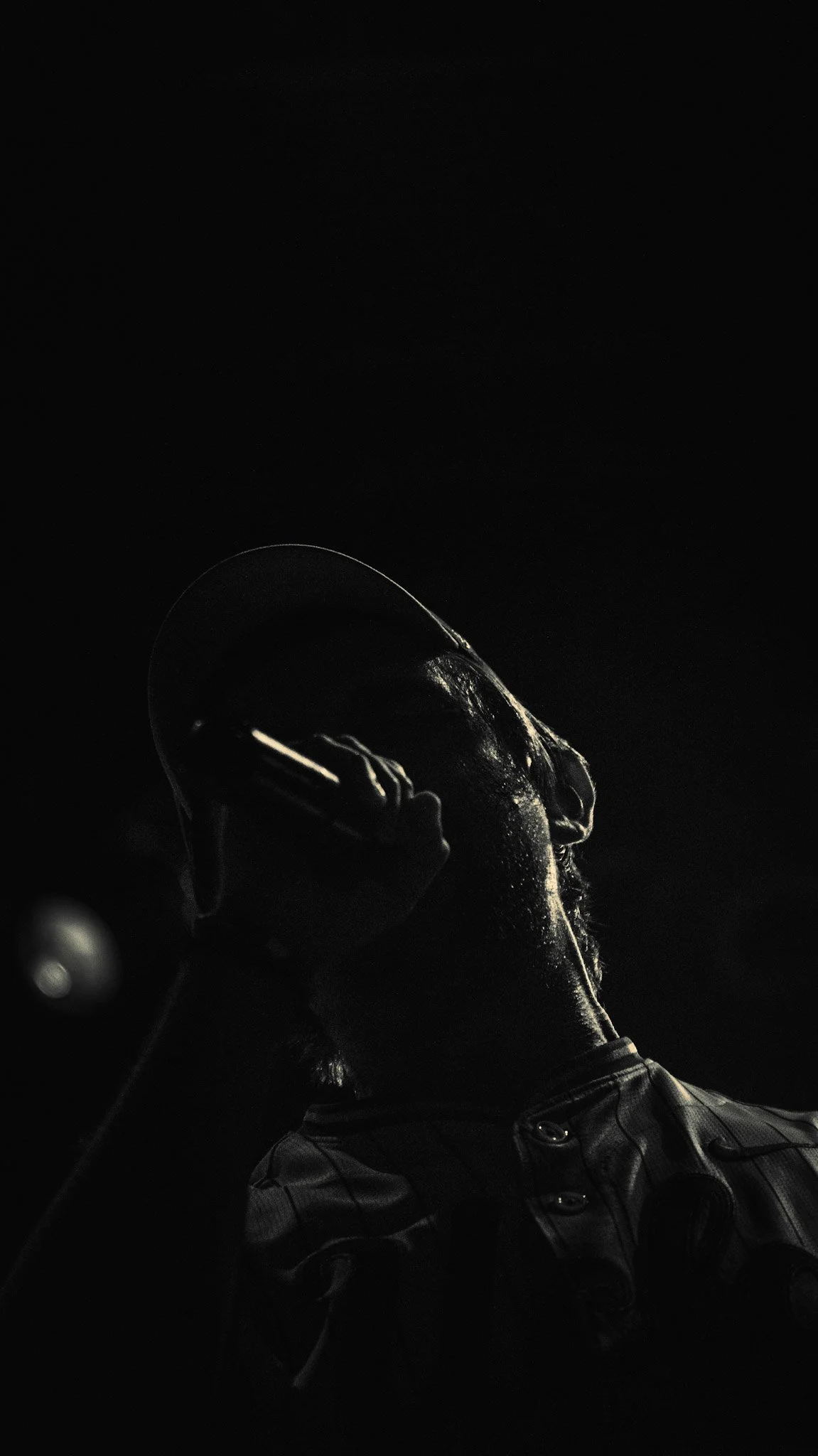 A person wearing a jacket is holding a microphone near their mouth, singing or speaking into it, with a dark background.