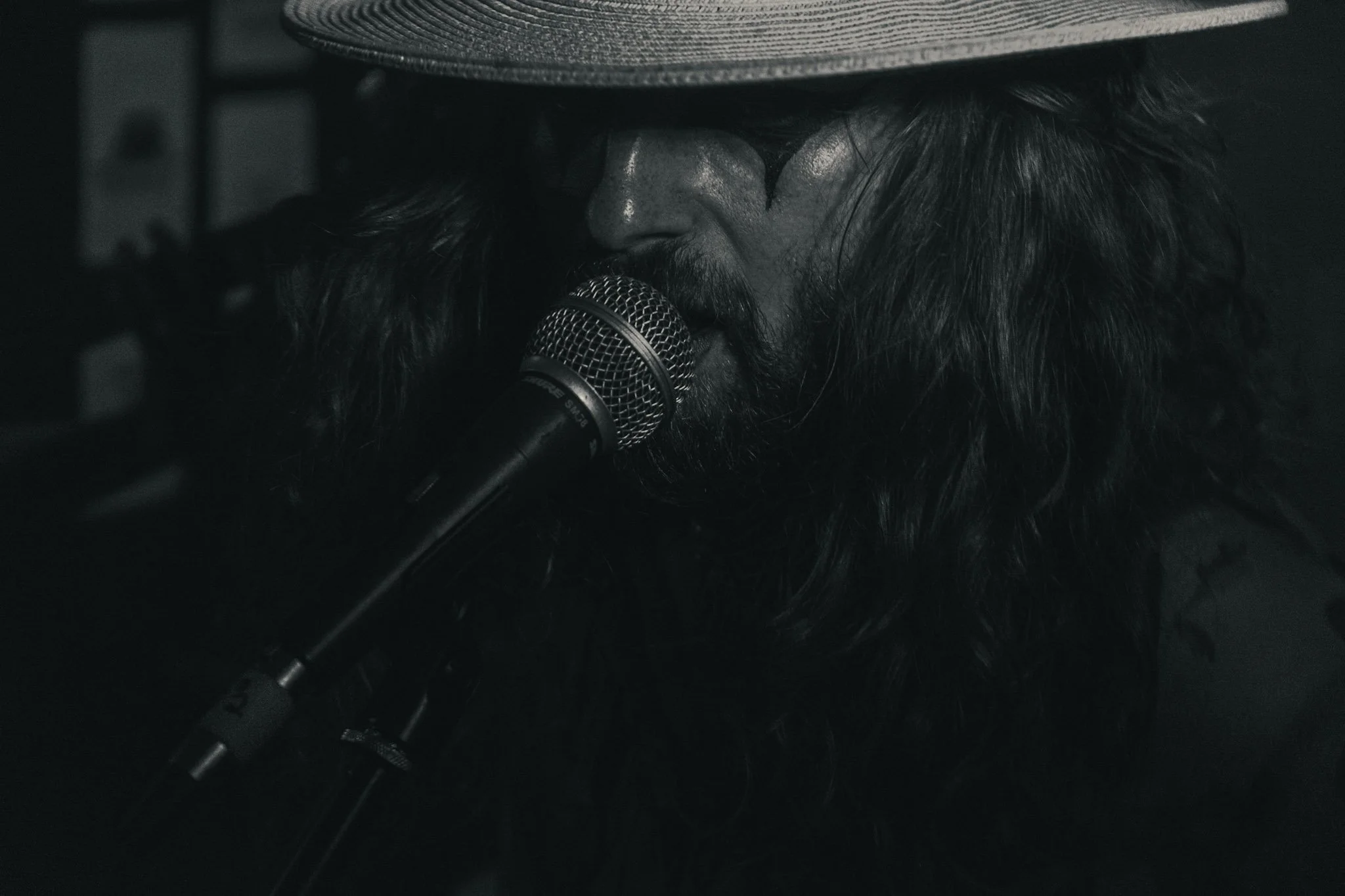 A man with long hair and a beard, wearing a wide-brimmed hat, singing into a microphone.