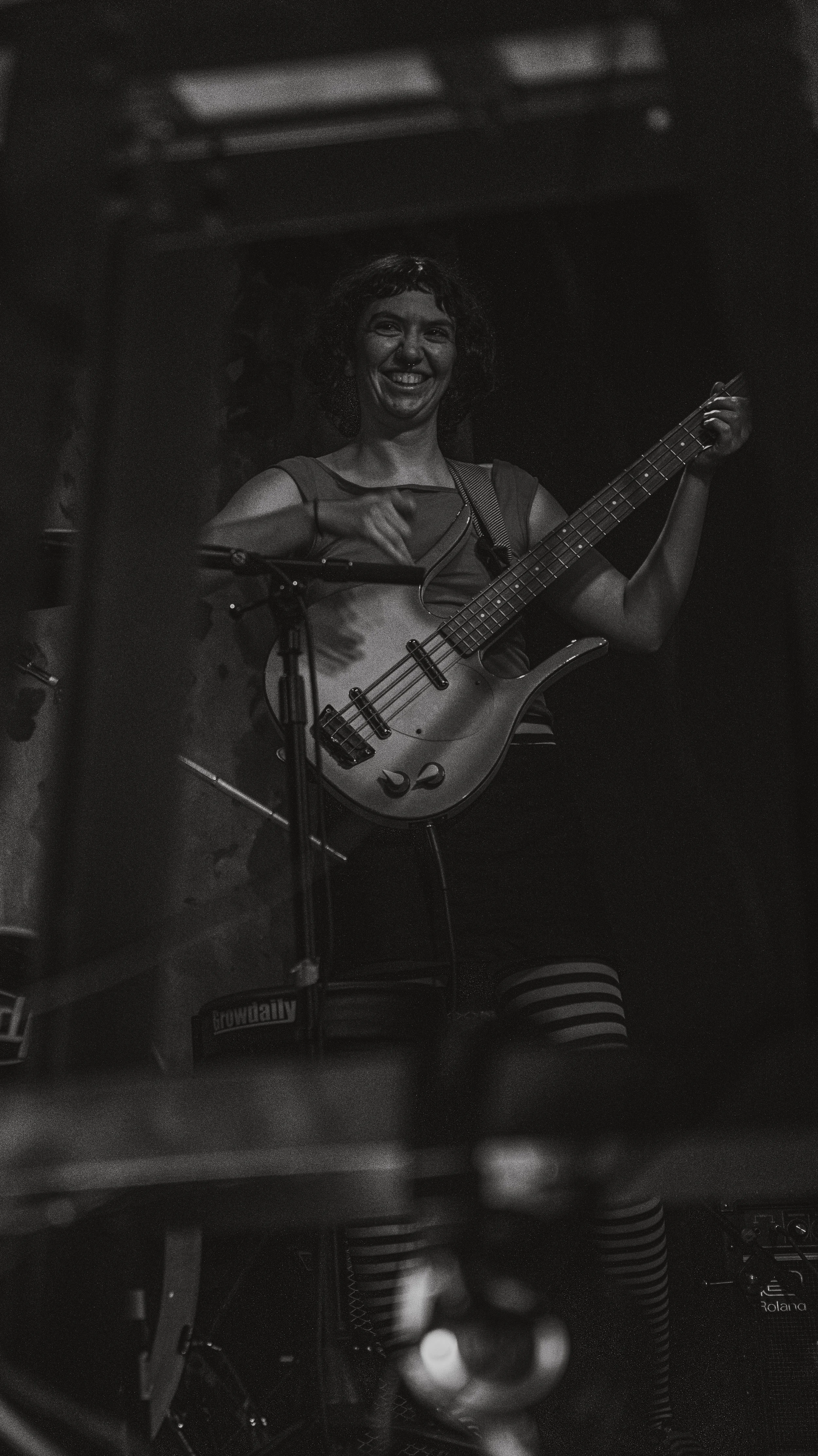 A woman smiling and playing a bass guitar on stage during a performance.