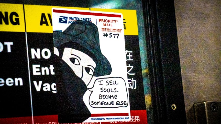 A sticker on a USPS Priority Mail box features an illustration of a dark figure with a broad-brimmed hat and a mask covering the lower face, with a speech bubble that says, 'I SELL SOULS. BECOME SOMEONE ELSE.'