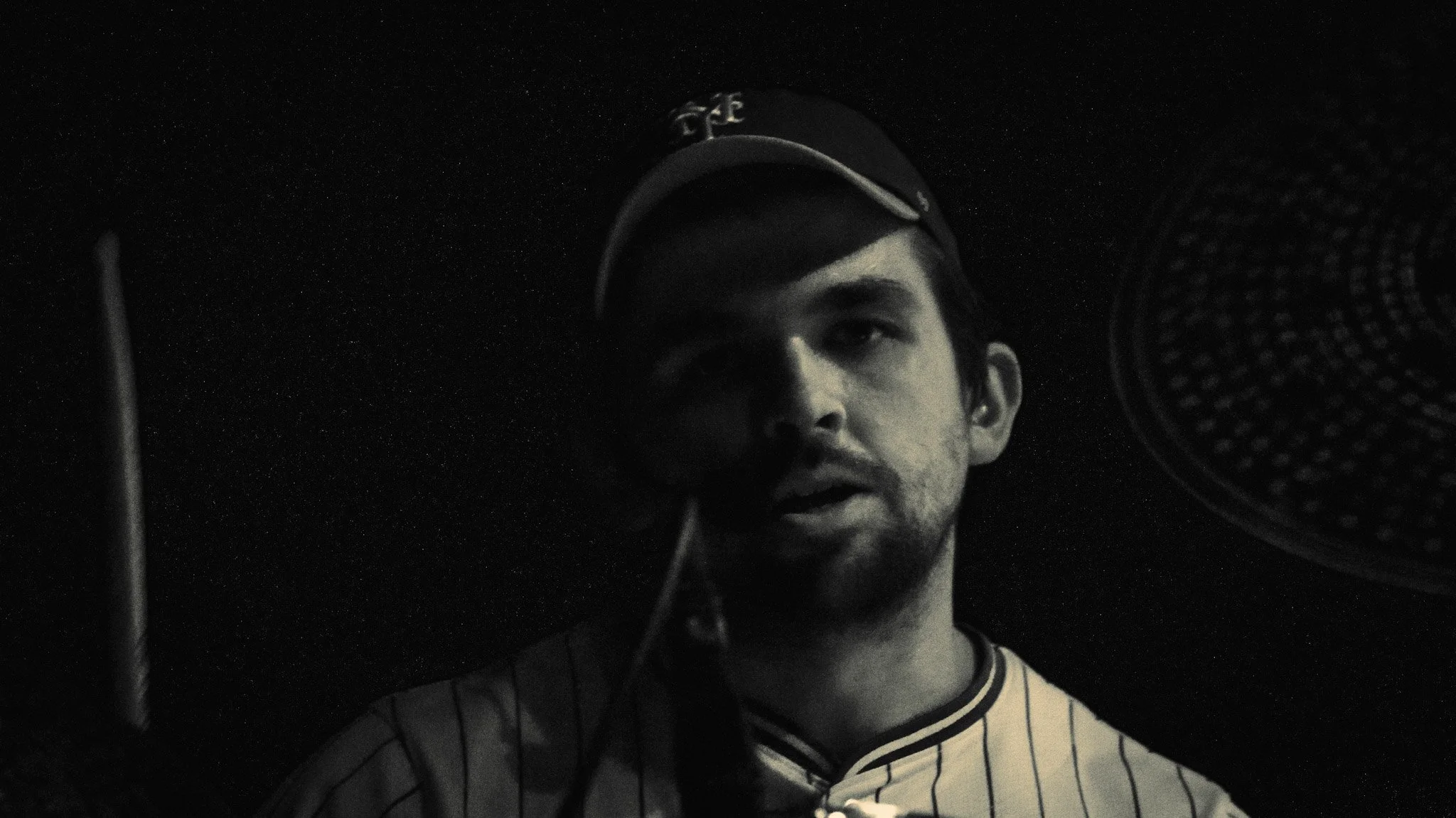 A young man recording vocals in a music studio, standing in front of a microphone, wearing a cap and striped shirt.