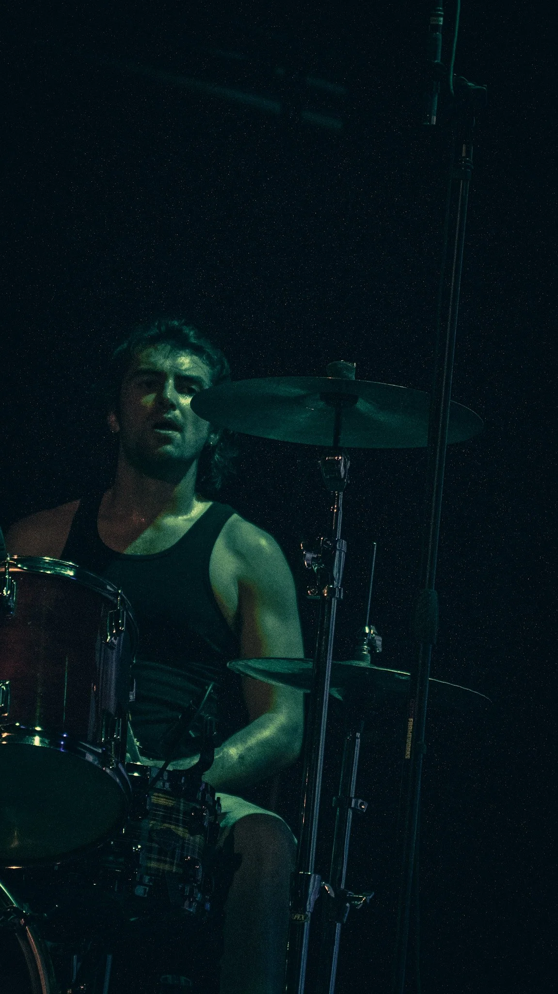 A young man playing the drums on a dark stage with a starry background.