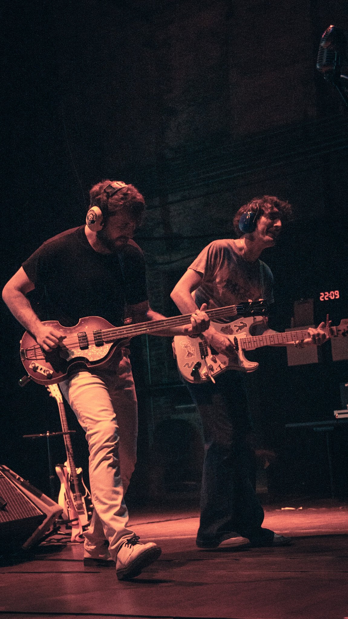 Two musicians playing guitars on stage in a dimly lit concert setting.