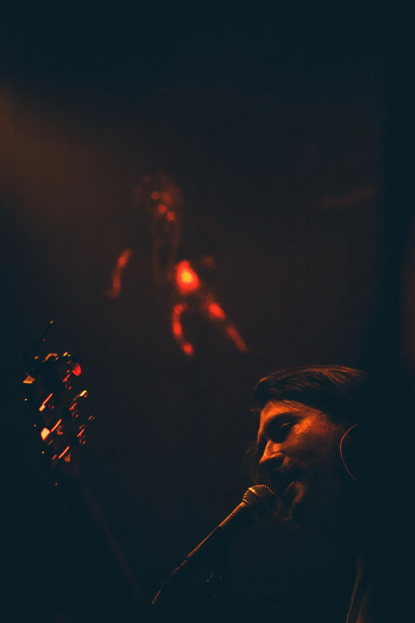 A woman with dark hair in a bun singing into a microphone during a dimly lit performance.
