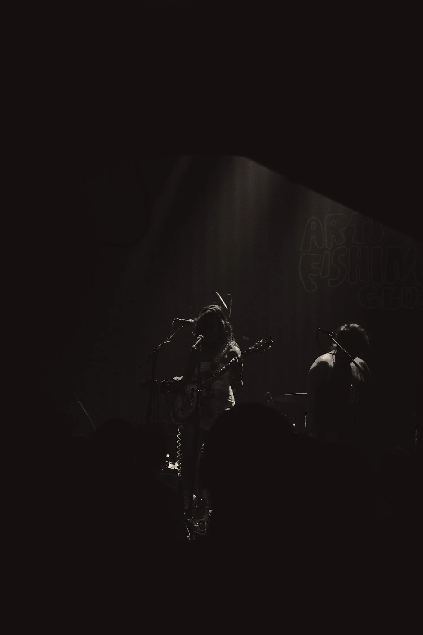 Musicians performing on stage with spotlight shining down, with a partially visible sign in the background reading 'ARTS FESTIVAL'