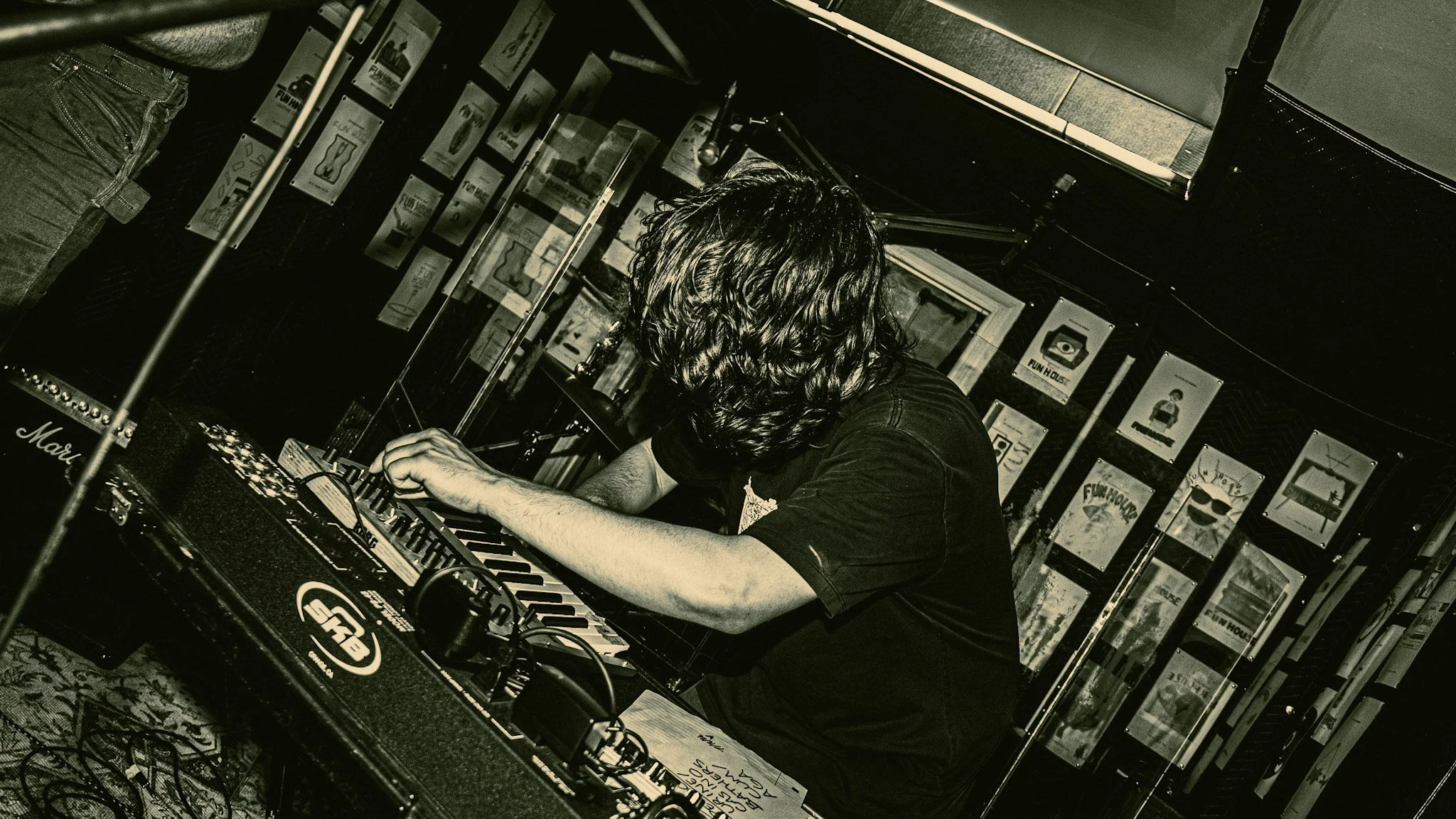 A person with long hair playing DJ equipment in a dimly lit room with posters on the wall.
