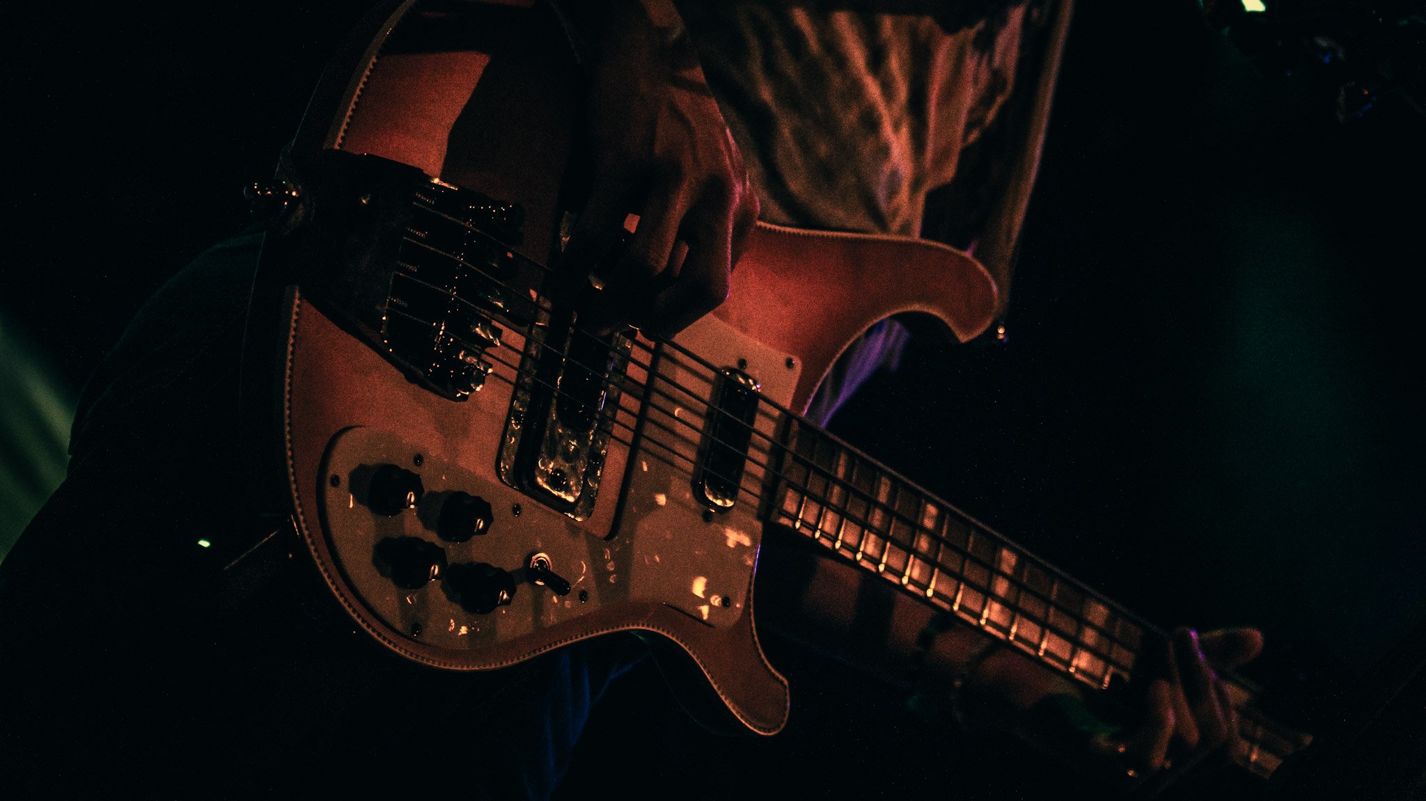 Close-up of an electric guitar being played in a dark setting, with a person's hand on the fretboard and strings visible.
