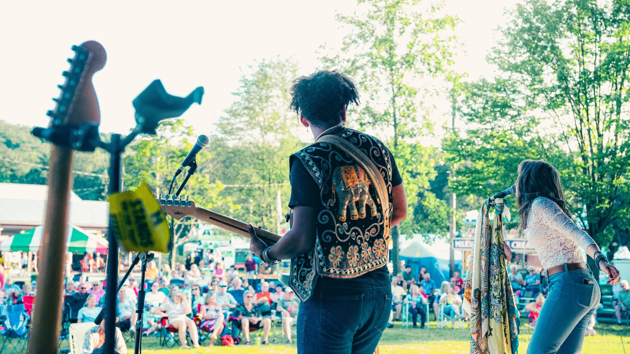 A musician playing guitar at an outdoor festival with crowd in the background