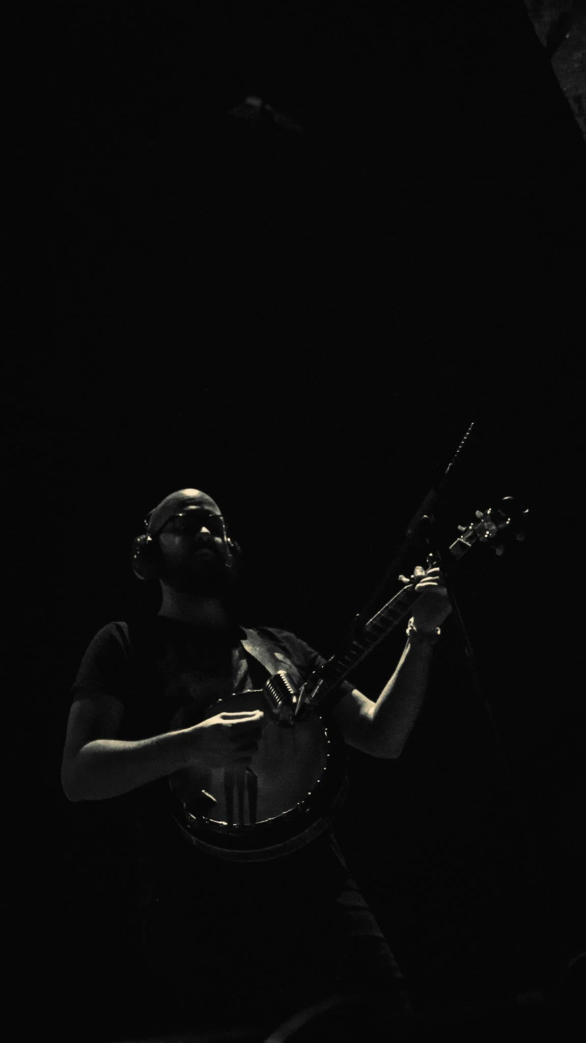 A person wearing a helmet, sunglasses, and headphones playing an electric guitar on a dark stage.