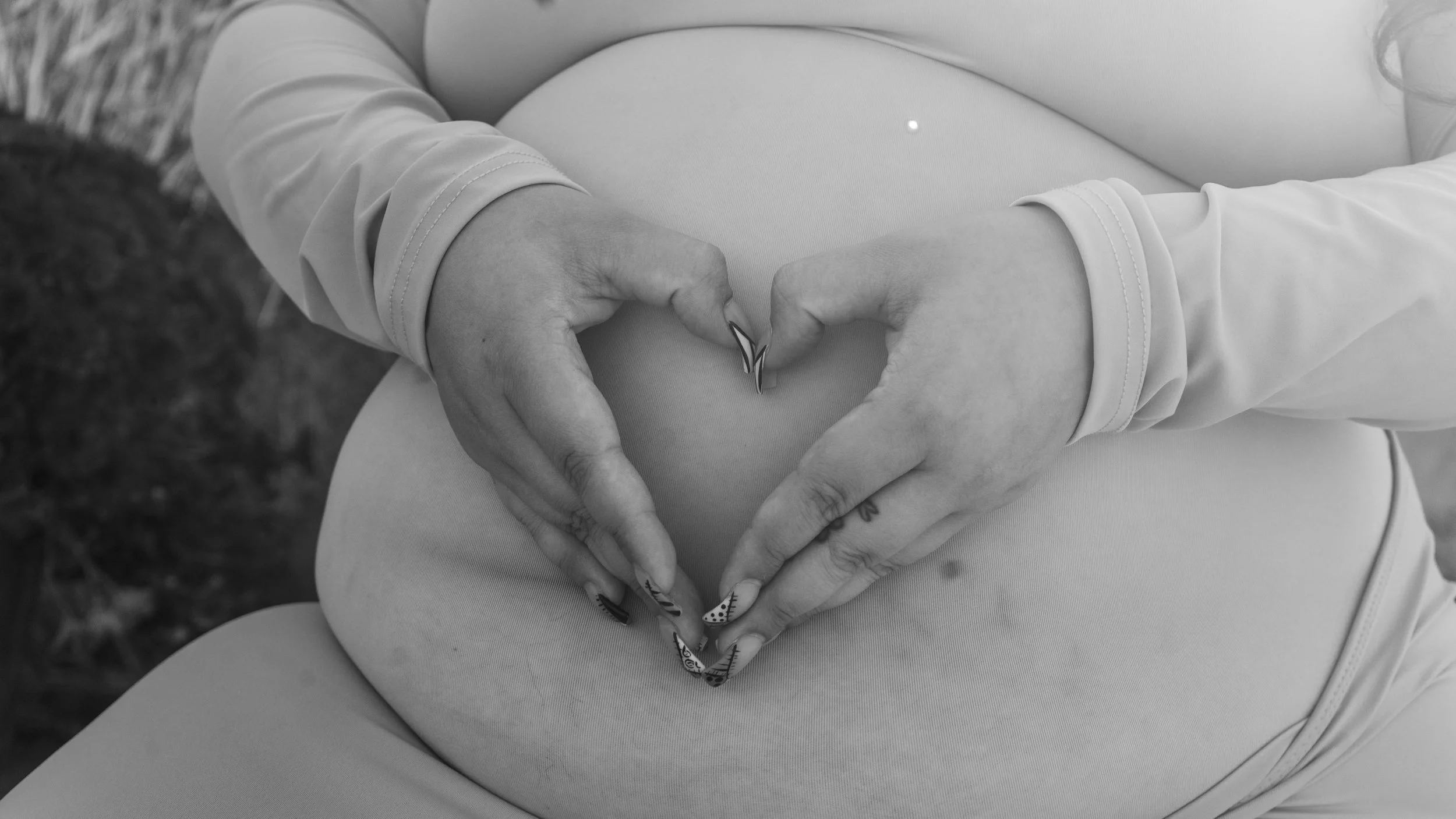 Black and white photo of a pregnant woman forming a heart shape with her hands on her belly.