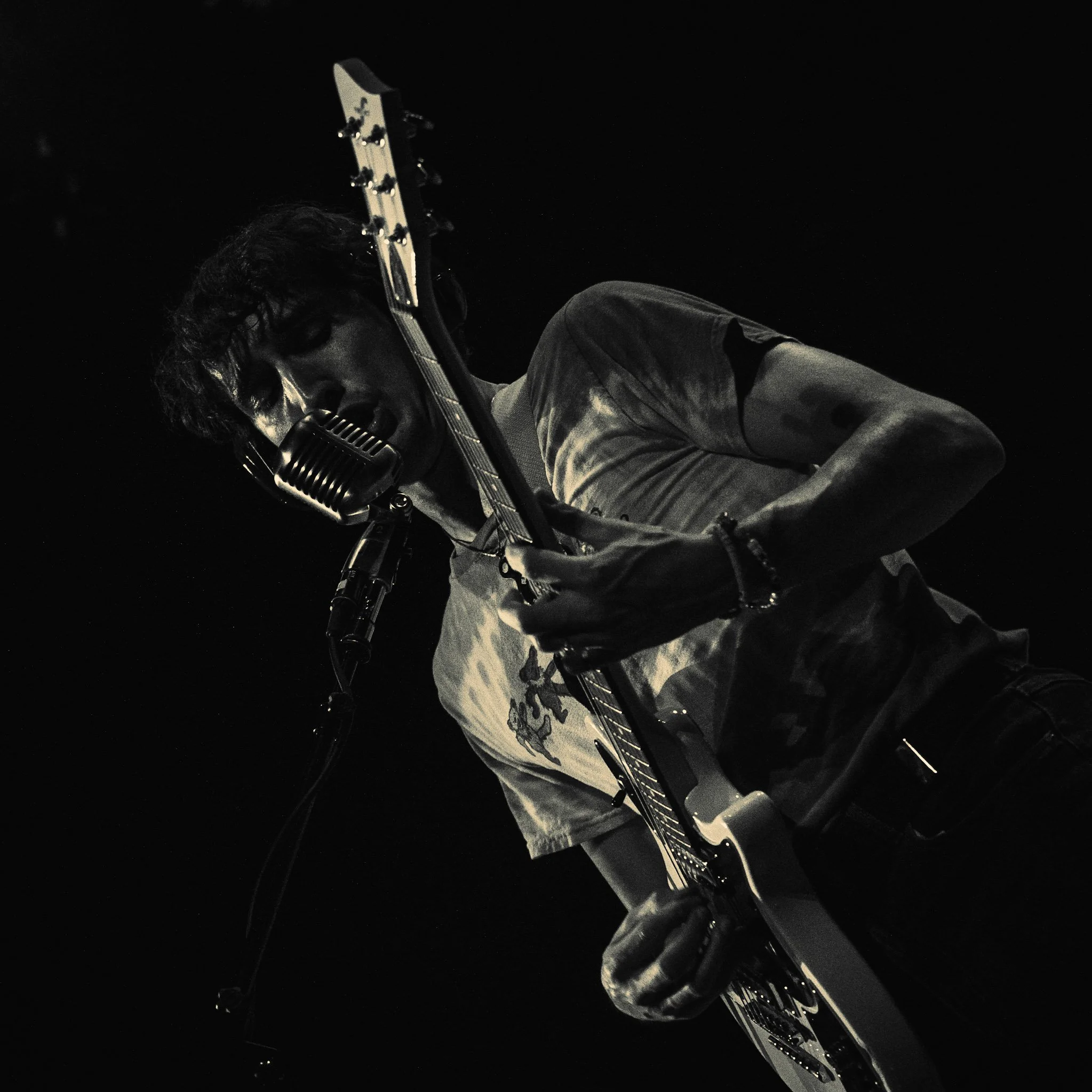 A man playing an electric guitar in a dimly lit setting, possibly at night or in a dark room.