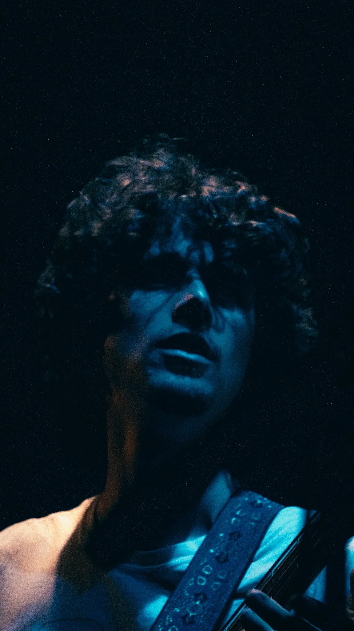 This is a portrait of a woman with curly hair, illuminated by blue light, holding a musical instrument, possibly a guitar, against a dark background with stars visible.