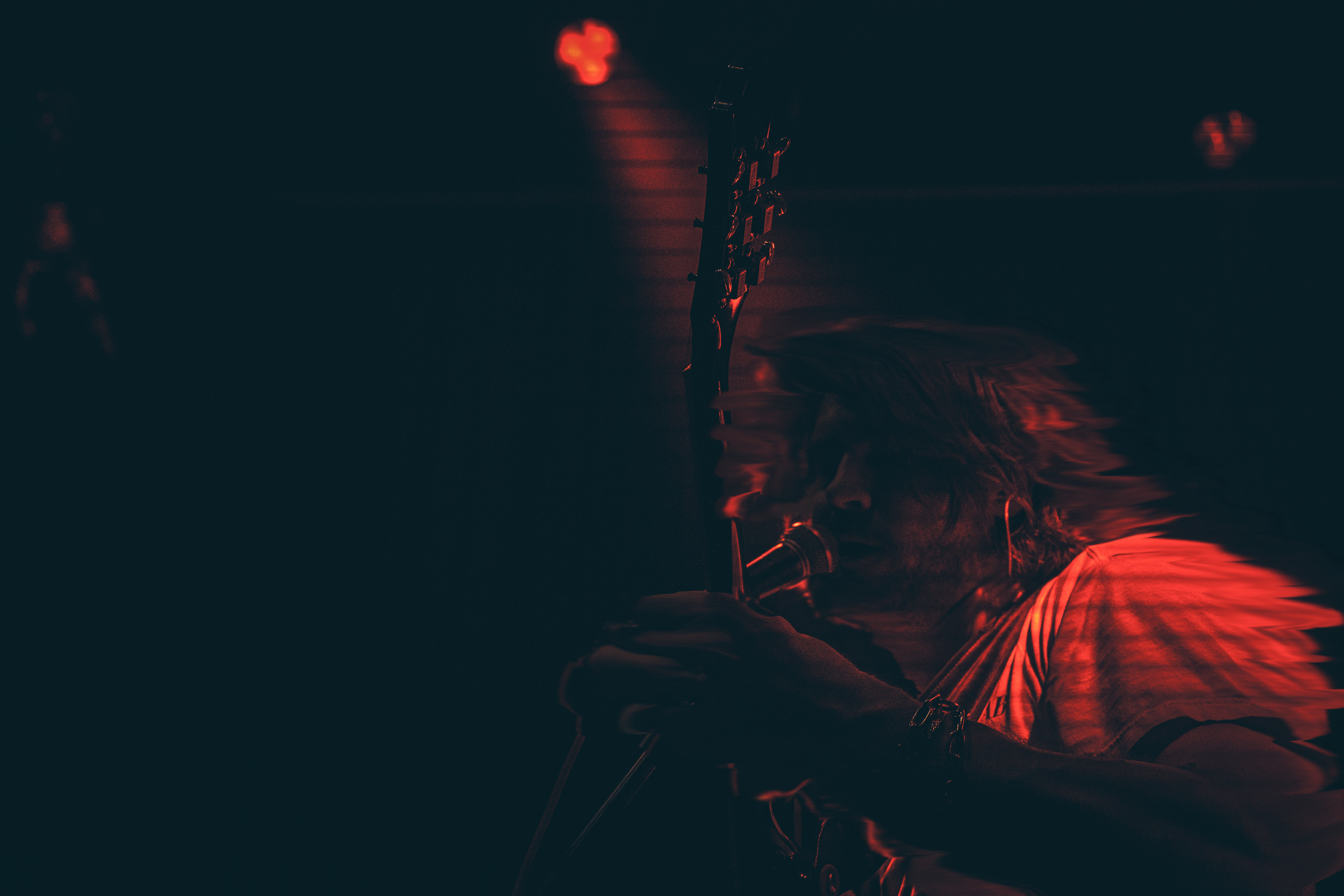 Close-up of an electric guitar viewed in a dark, moody setting with red lighting highlights.