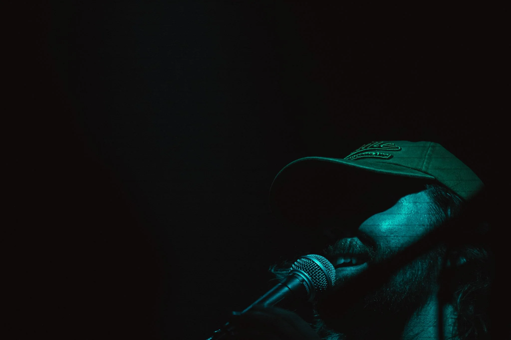 A hand wearing a green glove rests on a table with a microphone and a small object, against a dark background.