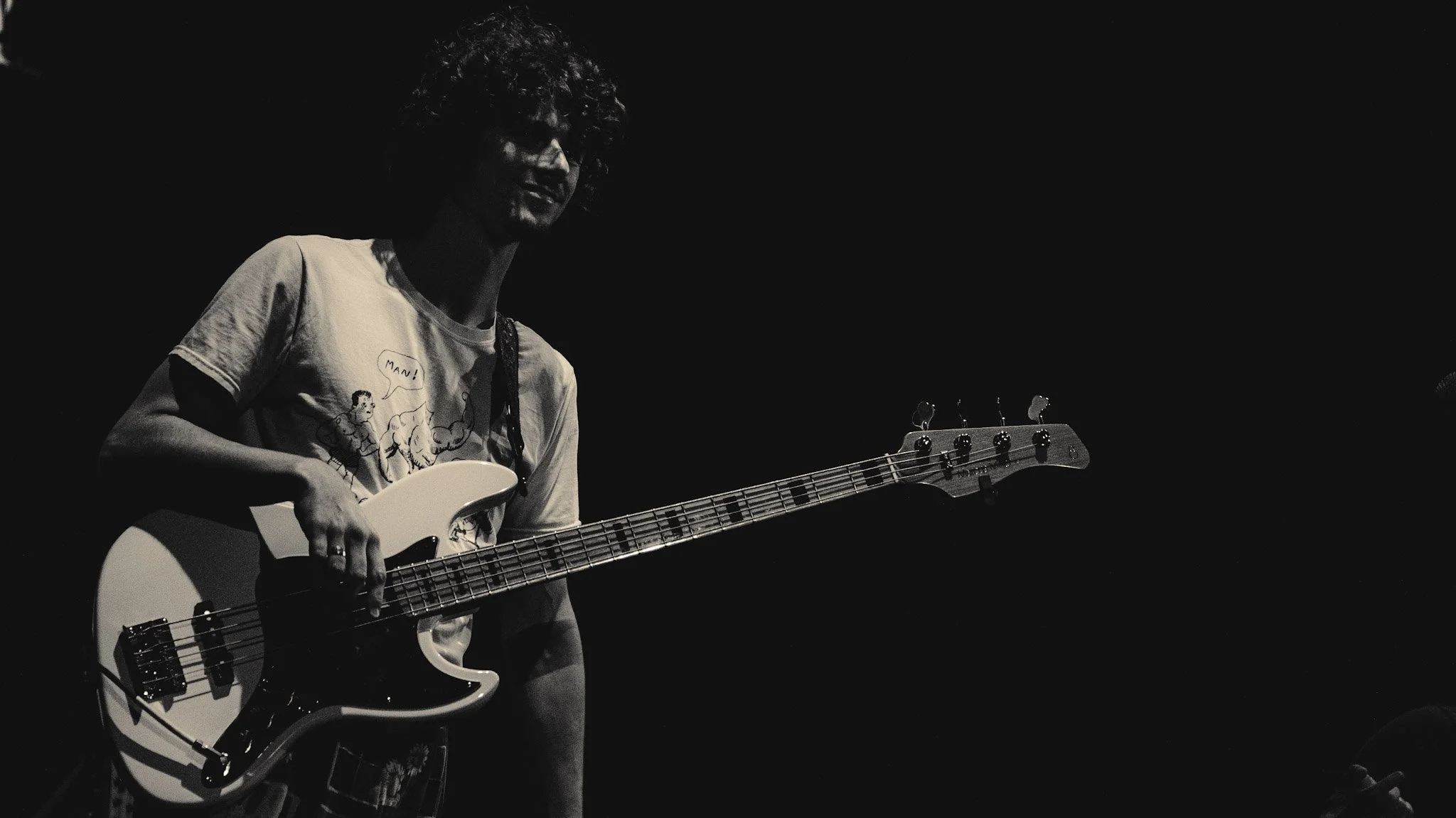 Person with curly hair playing an electric guitar in a dark setting