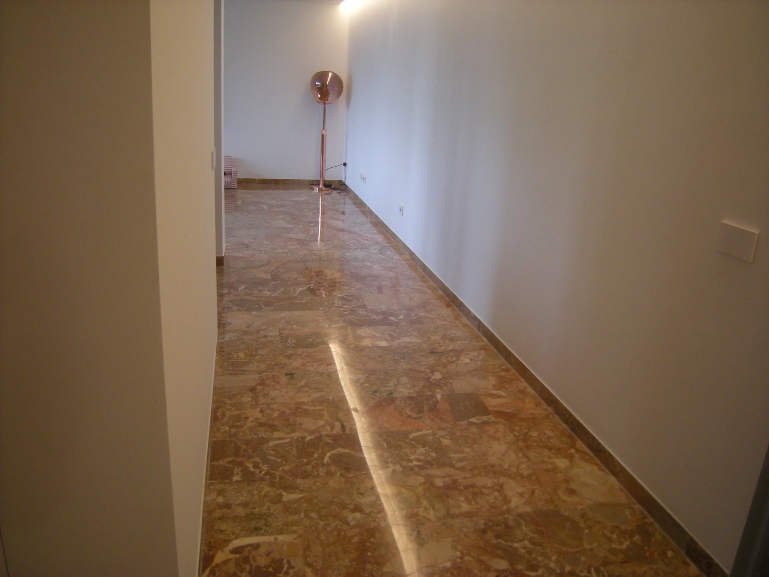 Ingresso di un appartamento con pareti bianche, pavimento in marmo marrone, lampada rose gold e pile di scatole di carta in fondo a sinistra.