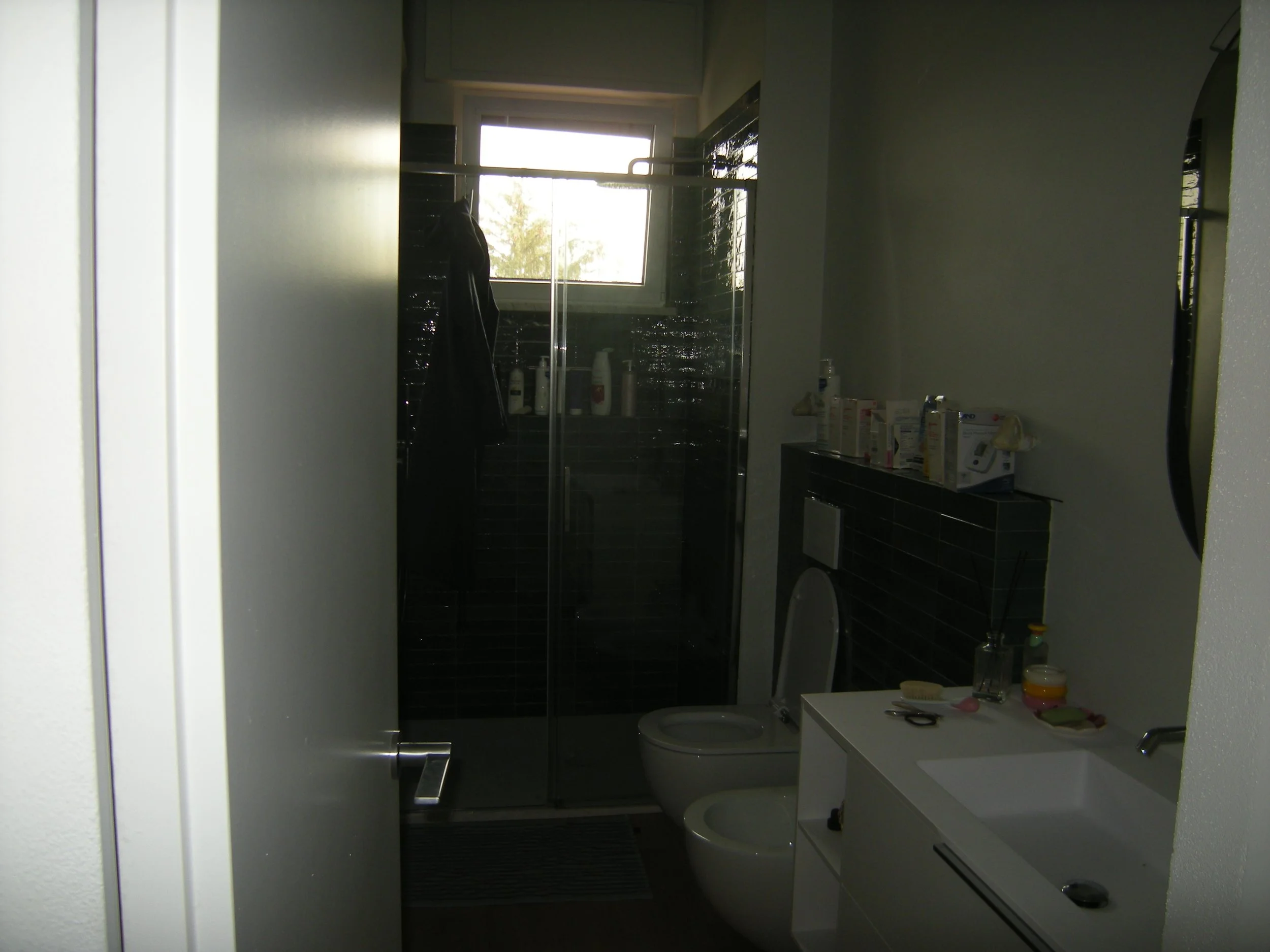 Bagno con finestra, box doccia, lavabo con alcuni oggetti, e WC, ambientato in modo semplice e moderno