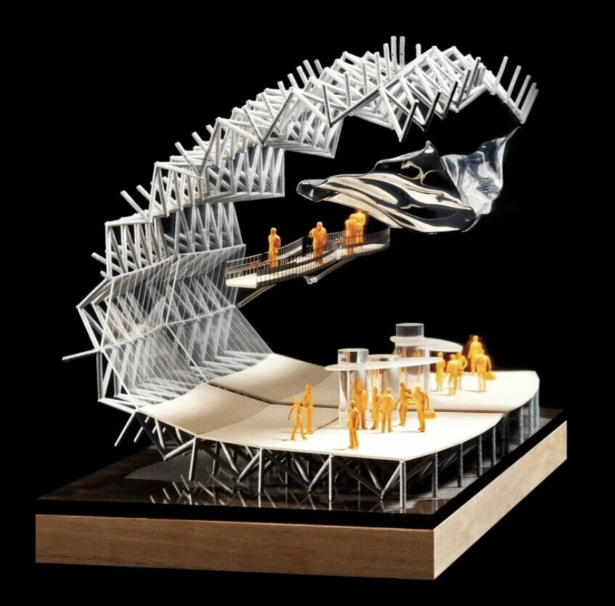 Architectural model of a modern multi-level venue with a curved structure, featuring a skateboard ramp, a walkway with orange miniature figures, and an upper deck with several miniature figures, all set against a black background.