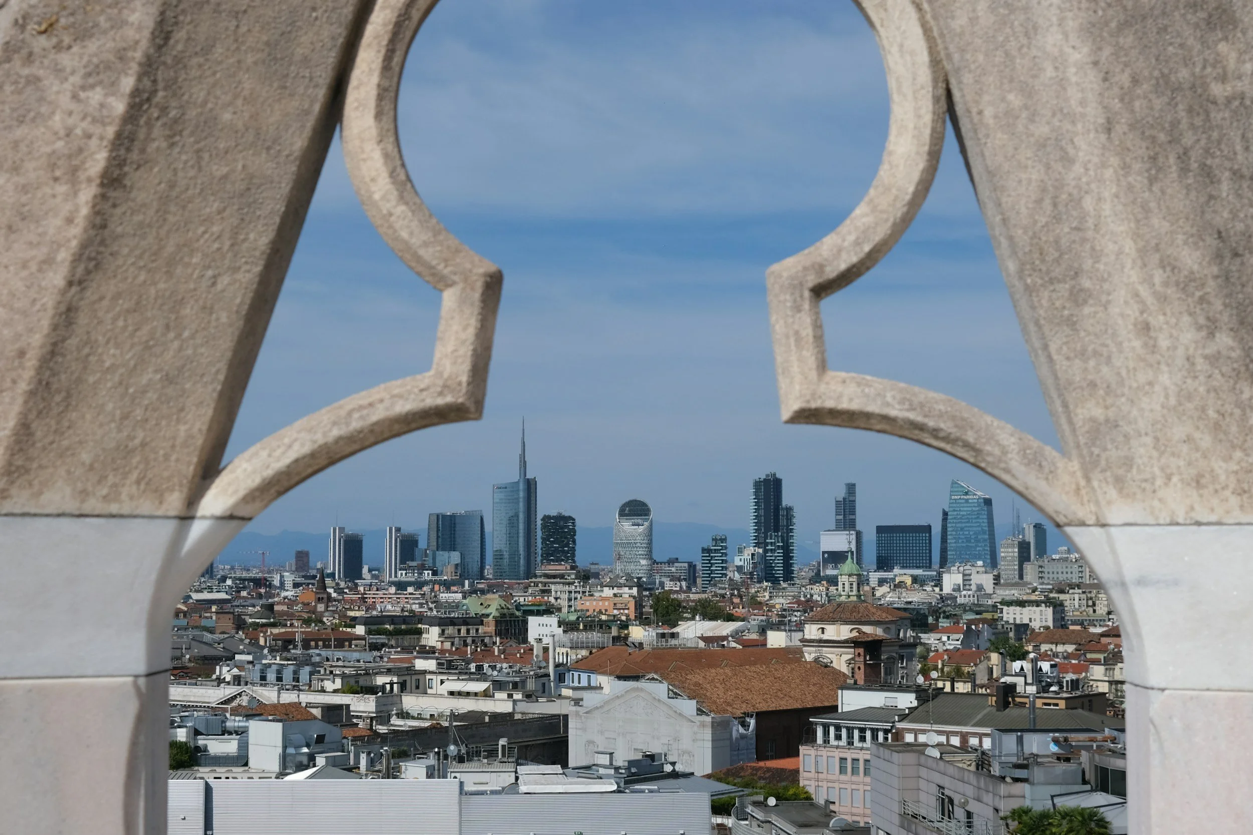 Veduta di un skyline cittadino con grattacieli moderni visti attraverso una finestra con un motivo di ferro decorativo in primo piano.