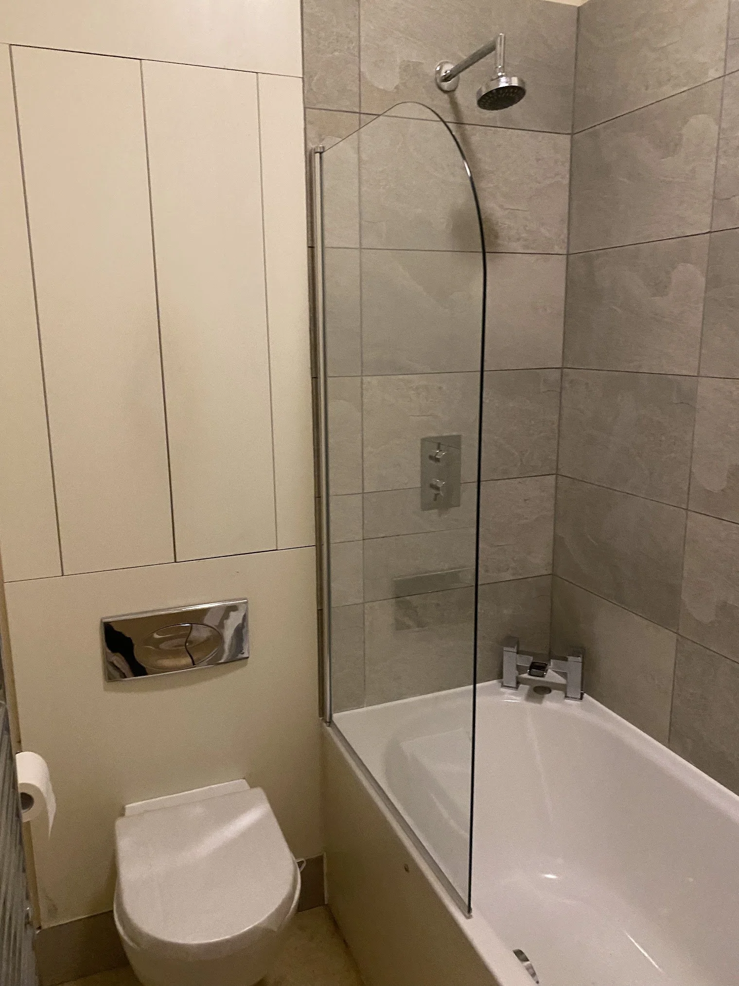 Bathroom with a toilet, a bathtub, a glass shower partition, and wall tiles in neutral colors.