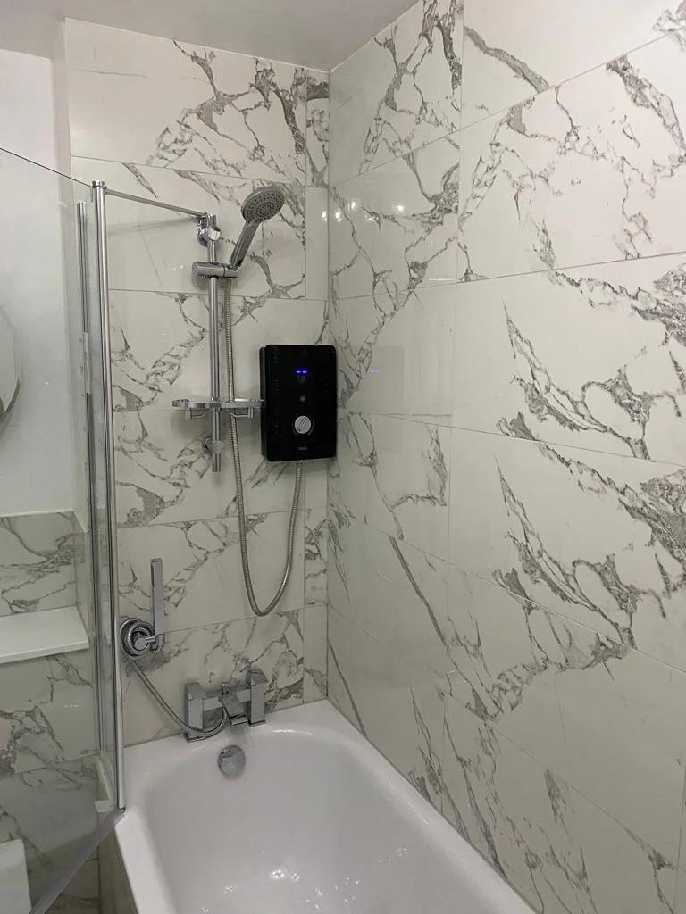 Bathroom shower area with marble tile walls, a black water heater, a handheld showerhead, and a white bathtub.