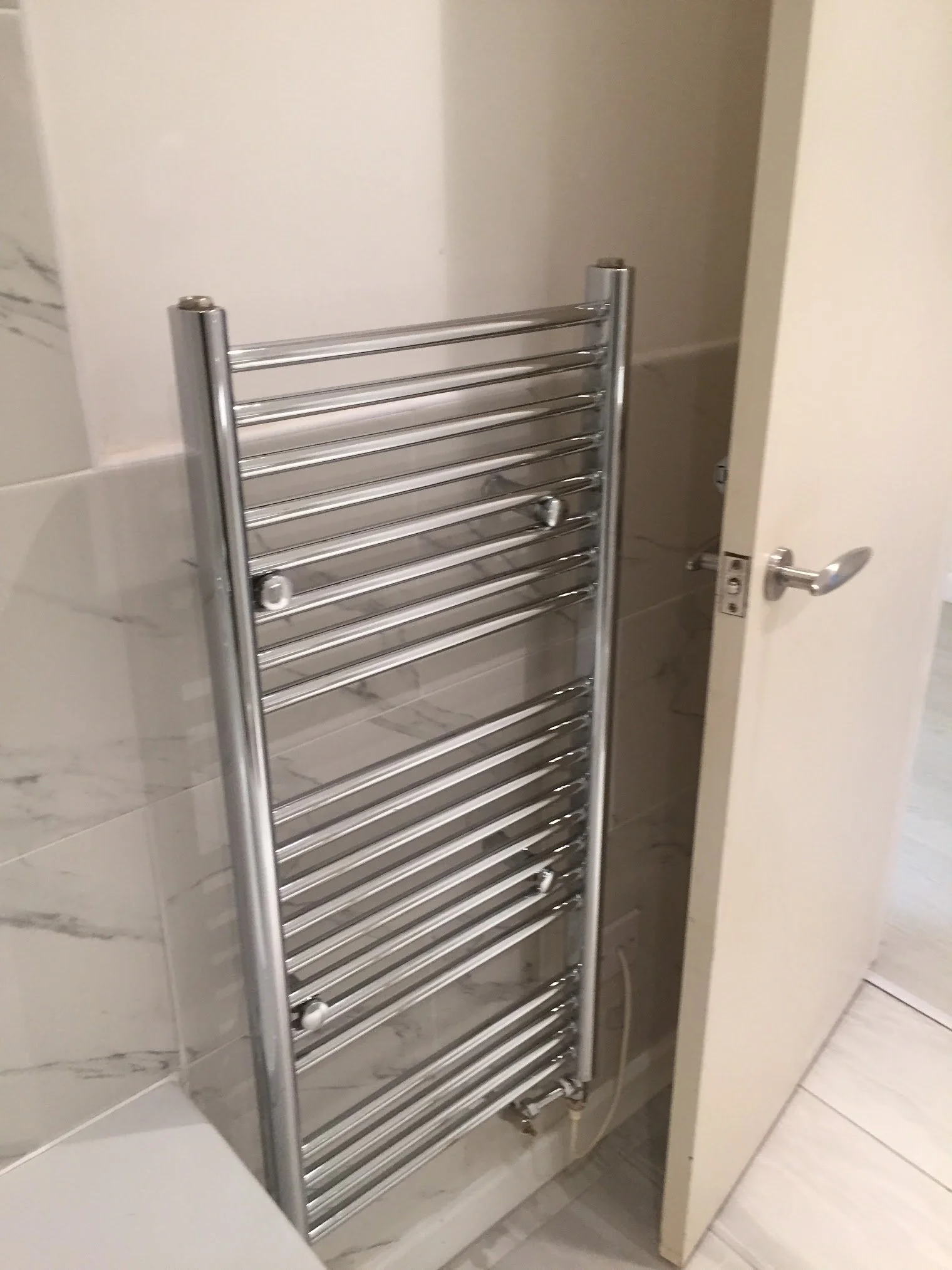 A heated towel rail mounted on a tiled bathroom wall, next to a door.
