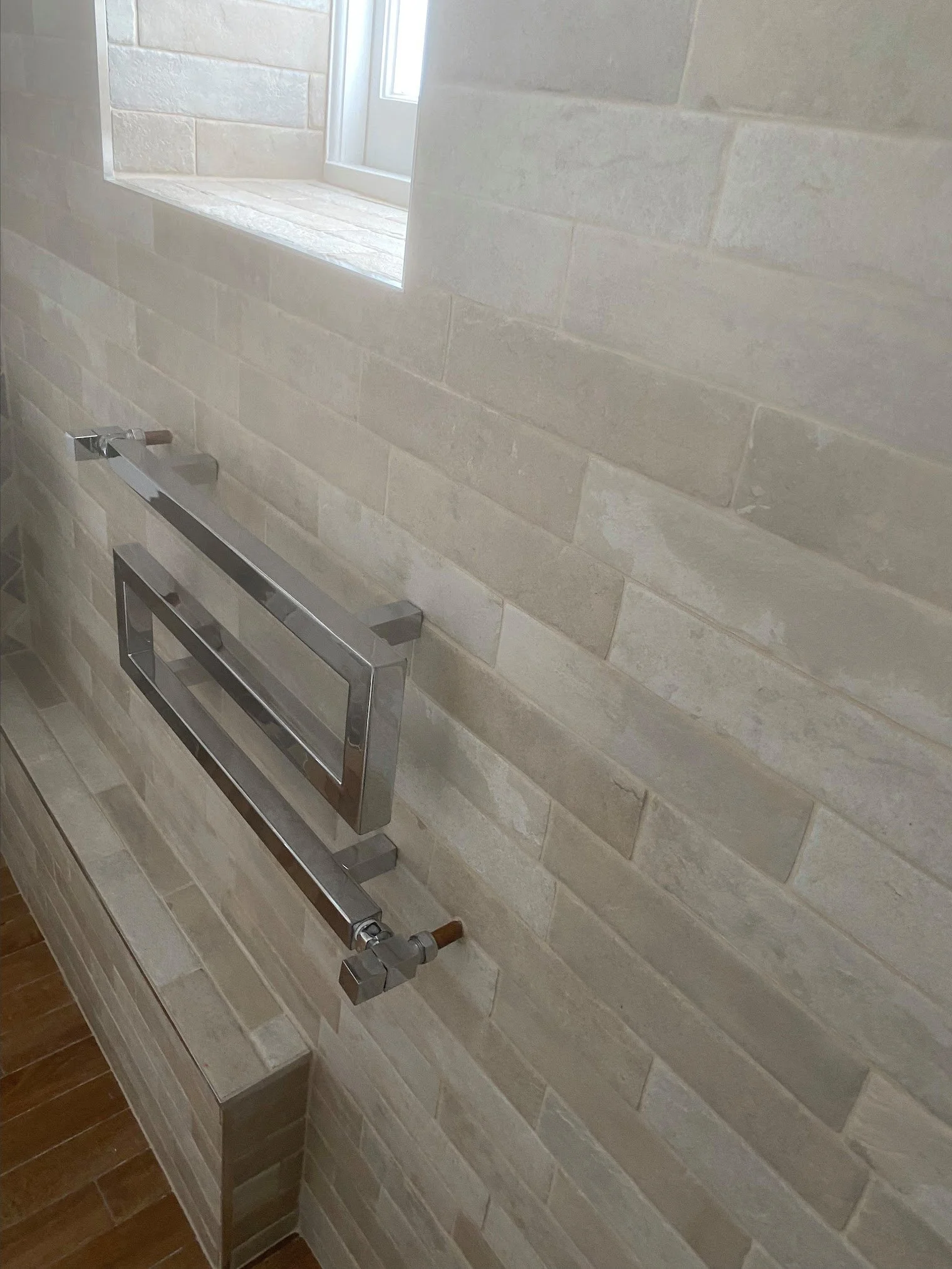 A wall with rectangular beige tiles and a chrome towel rack in a bathroom.