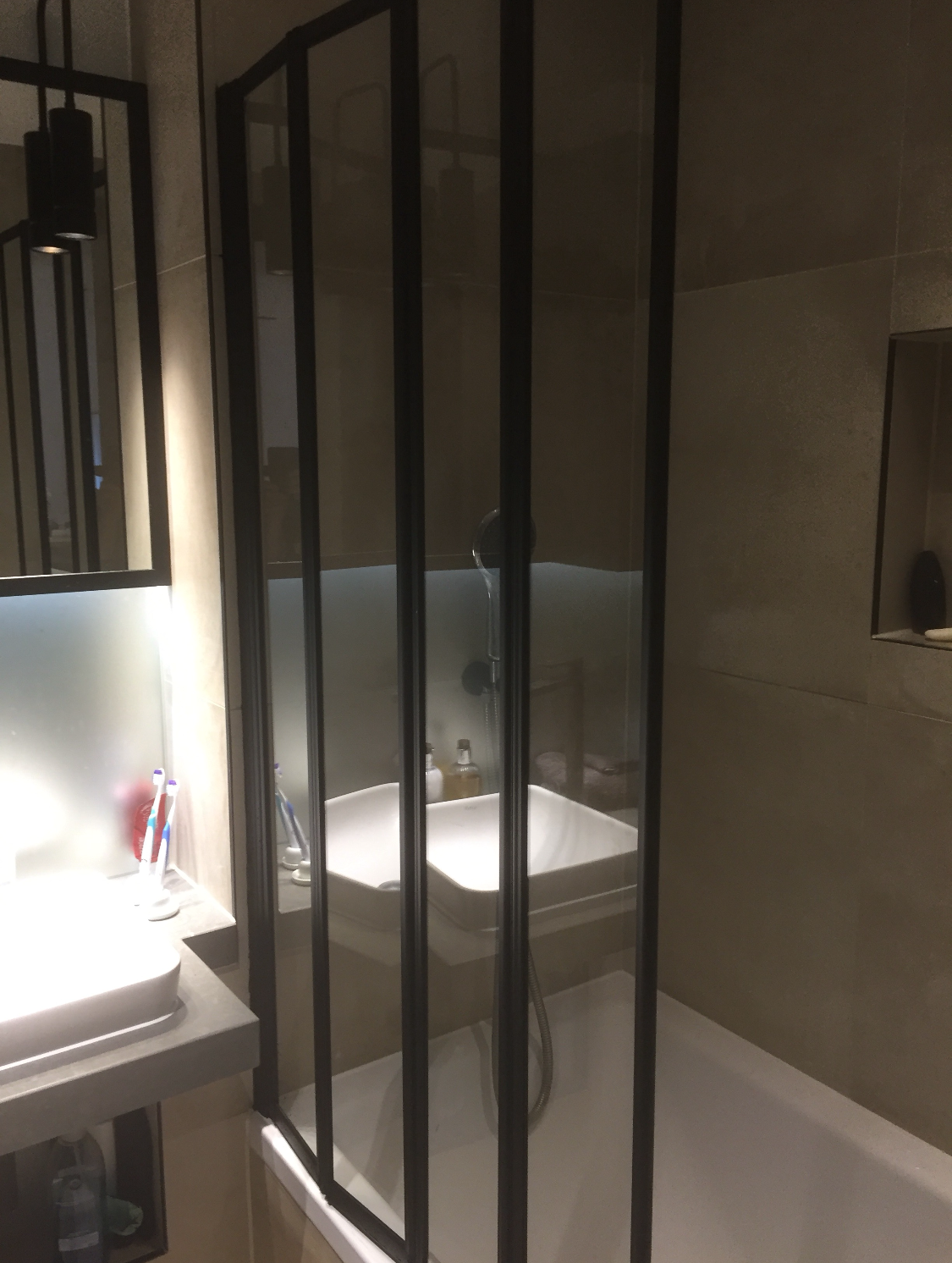 Bathroom with a walk-in shower, black metal frame, gray walls, white soaking tub, sink, toothbrushes, and toiletries.
