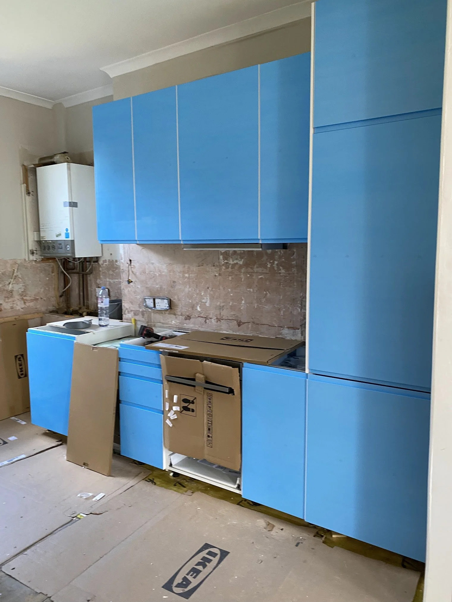 Blue kitchen cabinets being installed in a room under construction or renovation, with boxes and tools on the floor.